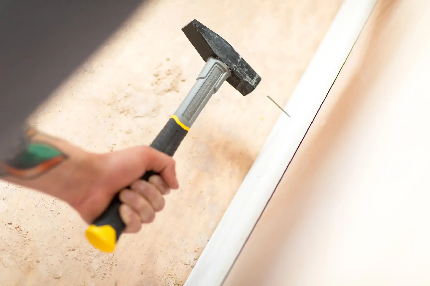 Photo of STANLEY STHT0-51908 hammer with yellow-black handle nailing trim against a wall.