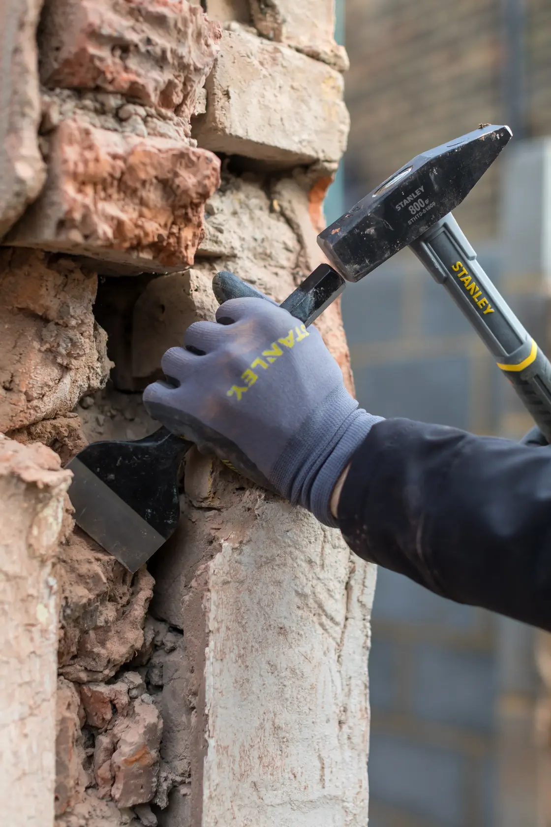 STANLEY STHT0-51909 photography of gloved hand using hammer and chisel to remove old mortar from brick wall.
