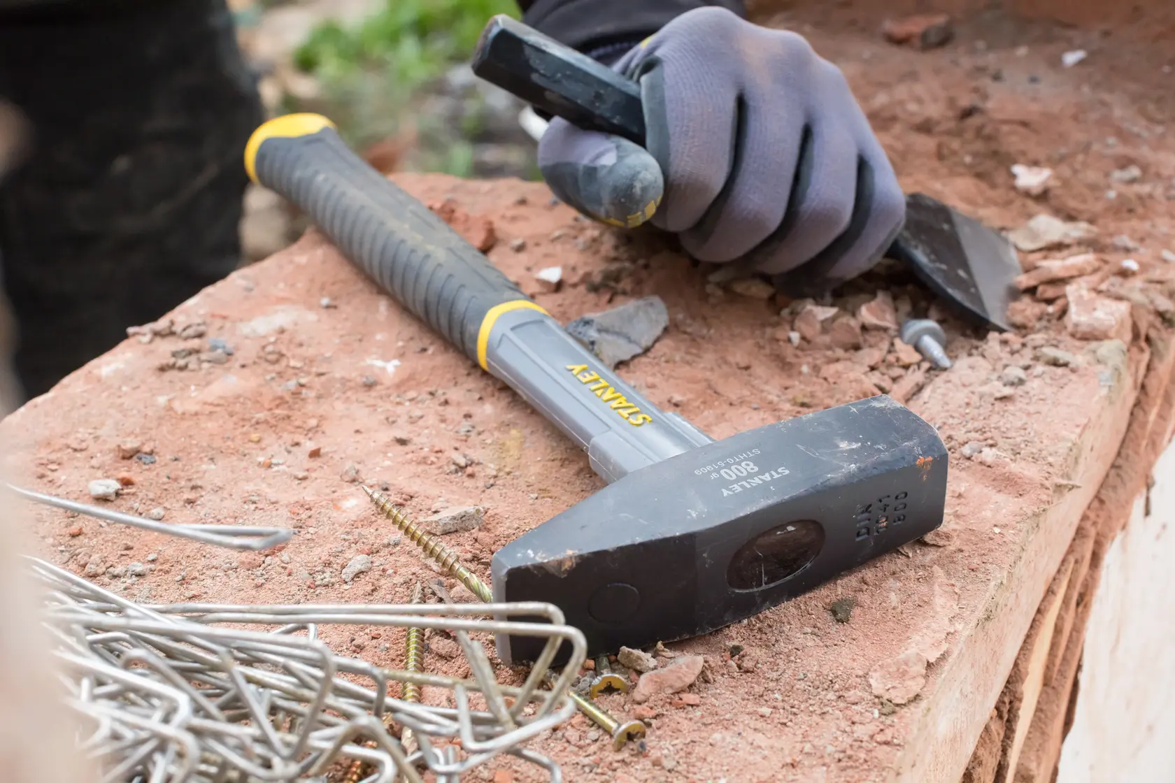 STANLEY STHT0-51909 sledge hammer with black handle on a workbench near metal fasteners and gloved hand.