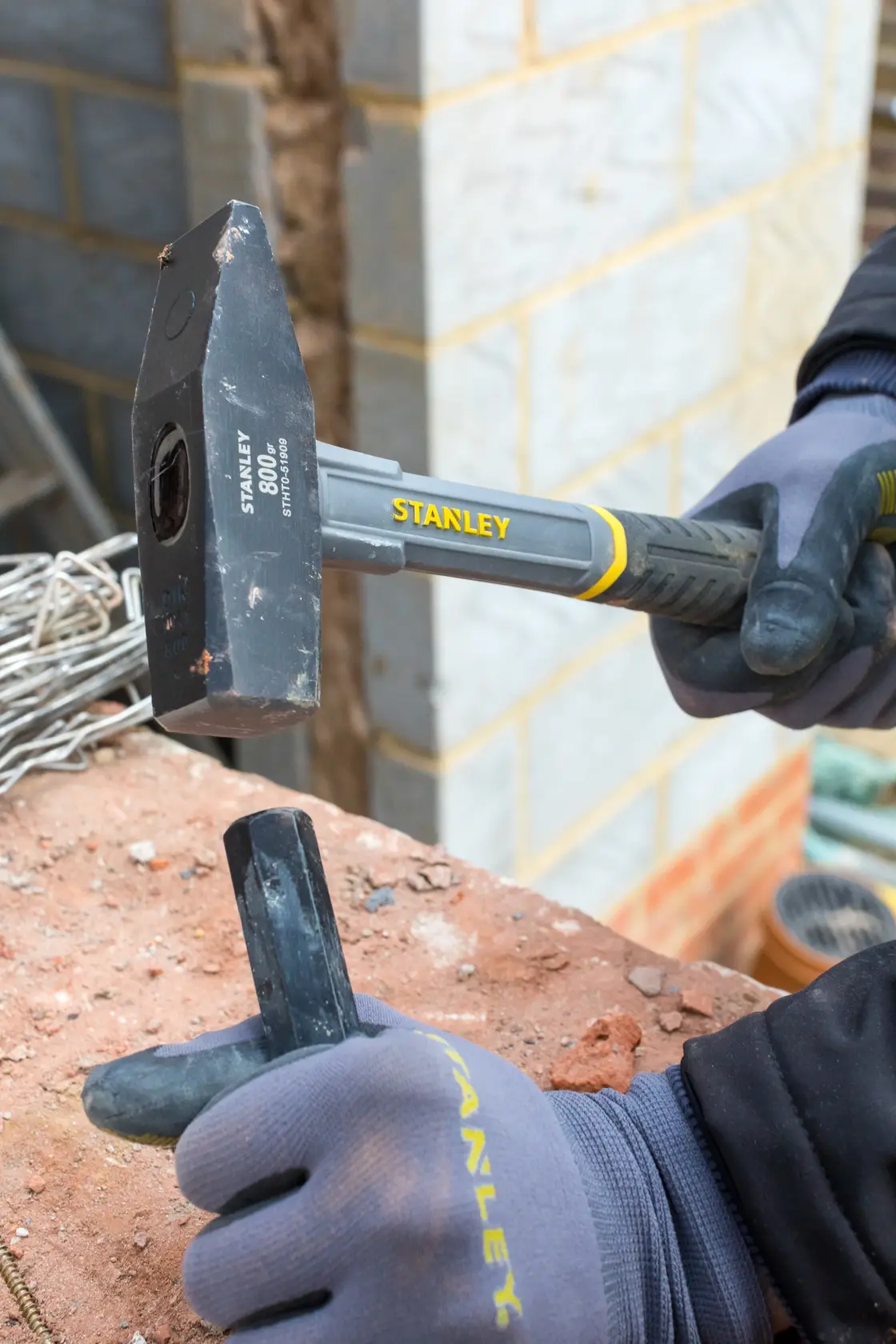 STANLEY STHT0-51909 club hammer with black-yellow handle in use on a brick, construction work context.