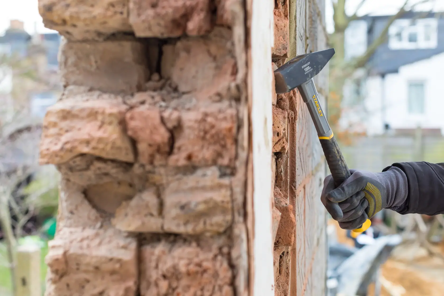 STANLEY STHT0-51910 brick hammer in use on masonry wall, close-up view, worker wearing gloves outdoors.