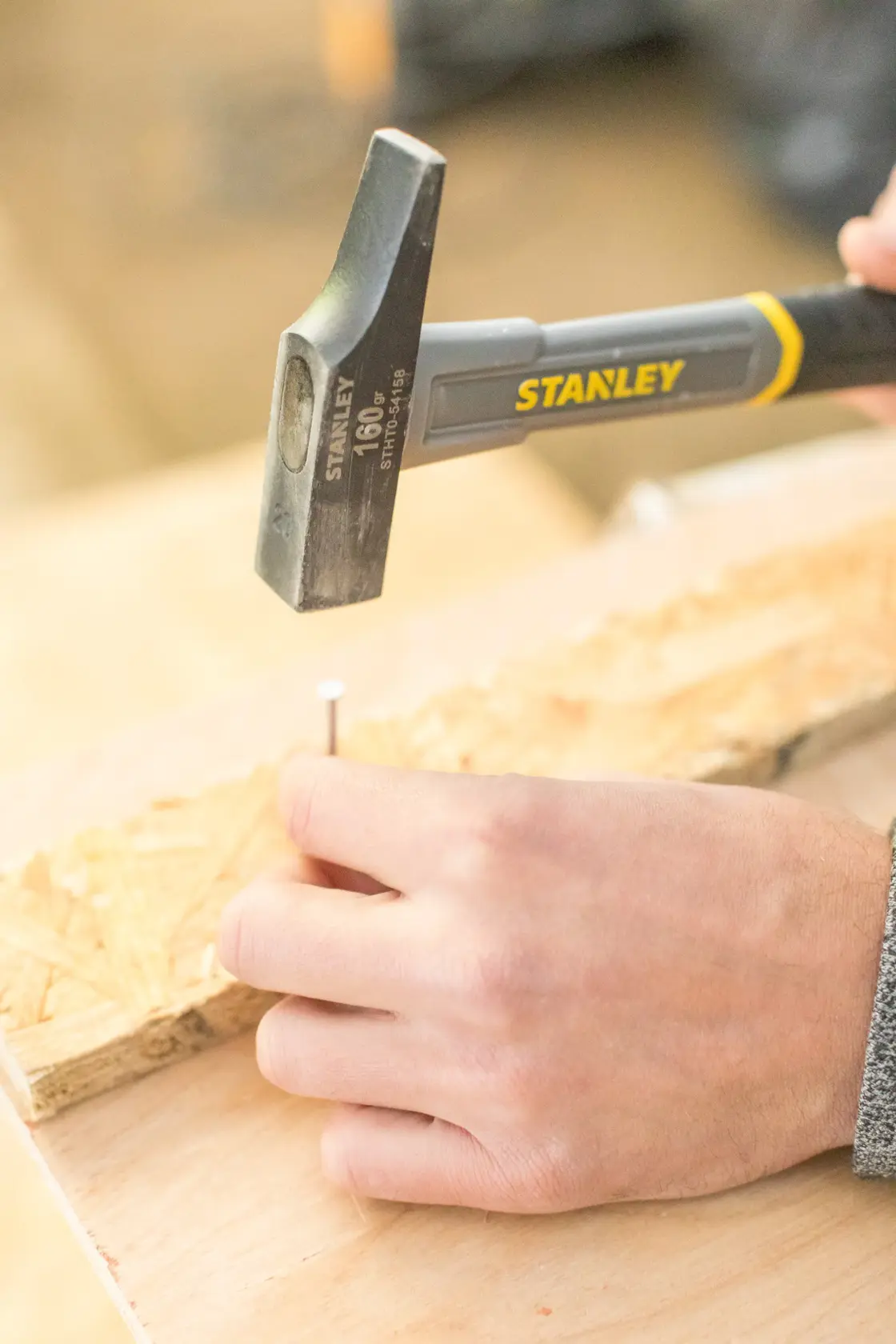 STANLEY STHT0-54158 claw hammer in use driving a nail into wood, close-up photography.