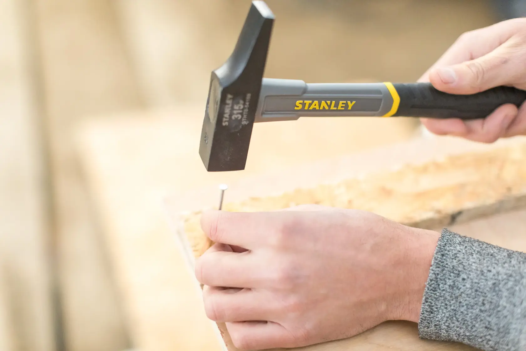 STANLEY STHT0-54159 hammer used to drive a nail into wood, close-up photography of hand tool in action.