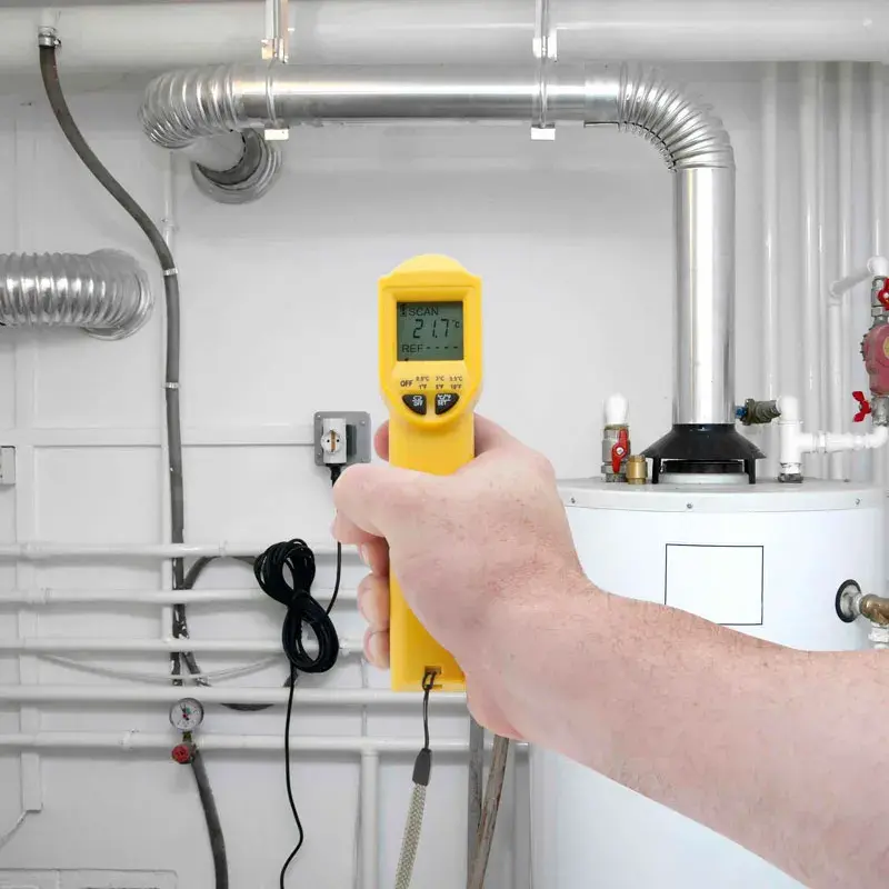 Photo of STANLEY STHT0-77365 digital thermometer held in hand, measuring temperature near industrial pipes.
