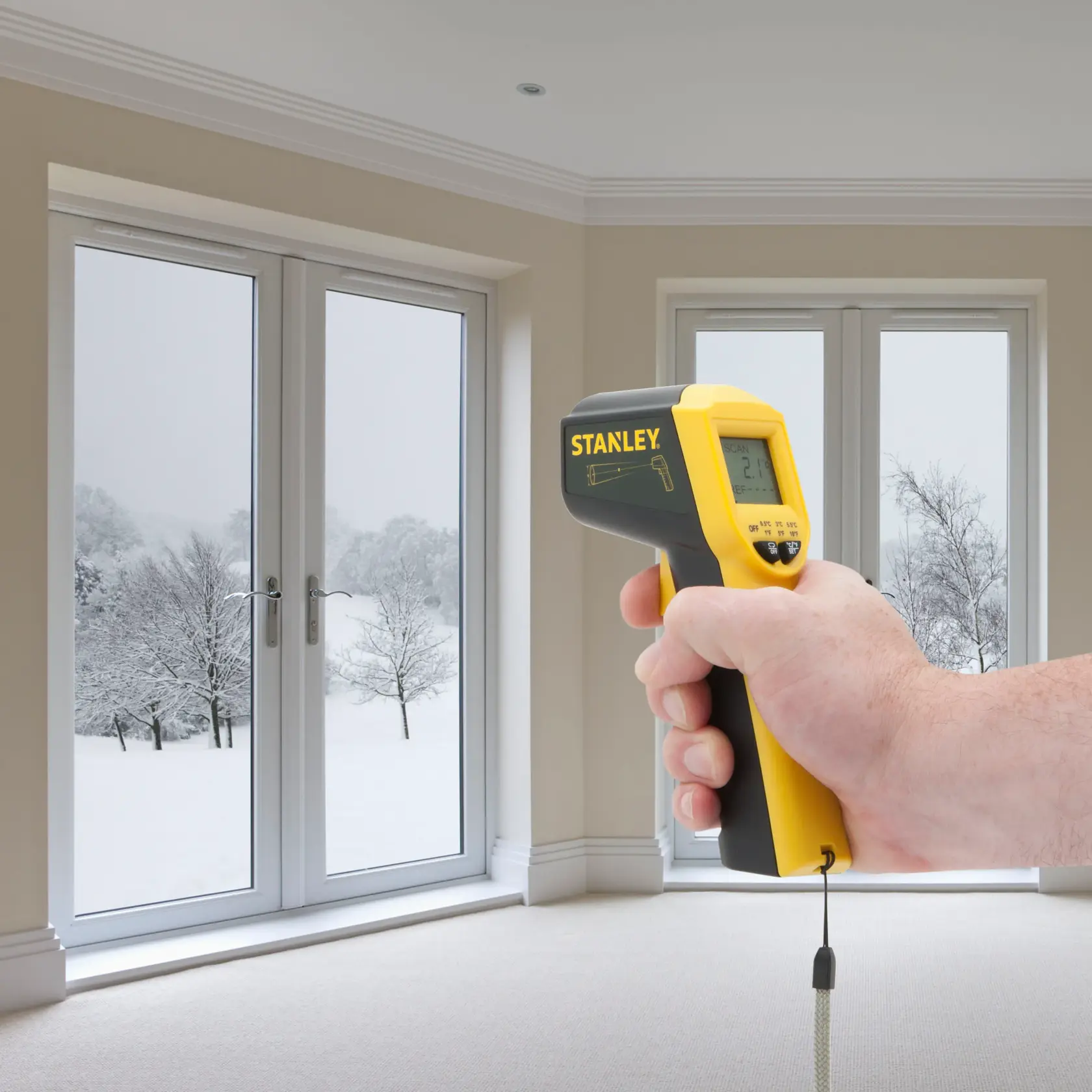 Stanley STHT0-77365 infrared thermometer held in hand, measuring window temperature indoors.