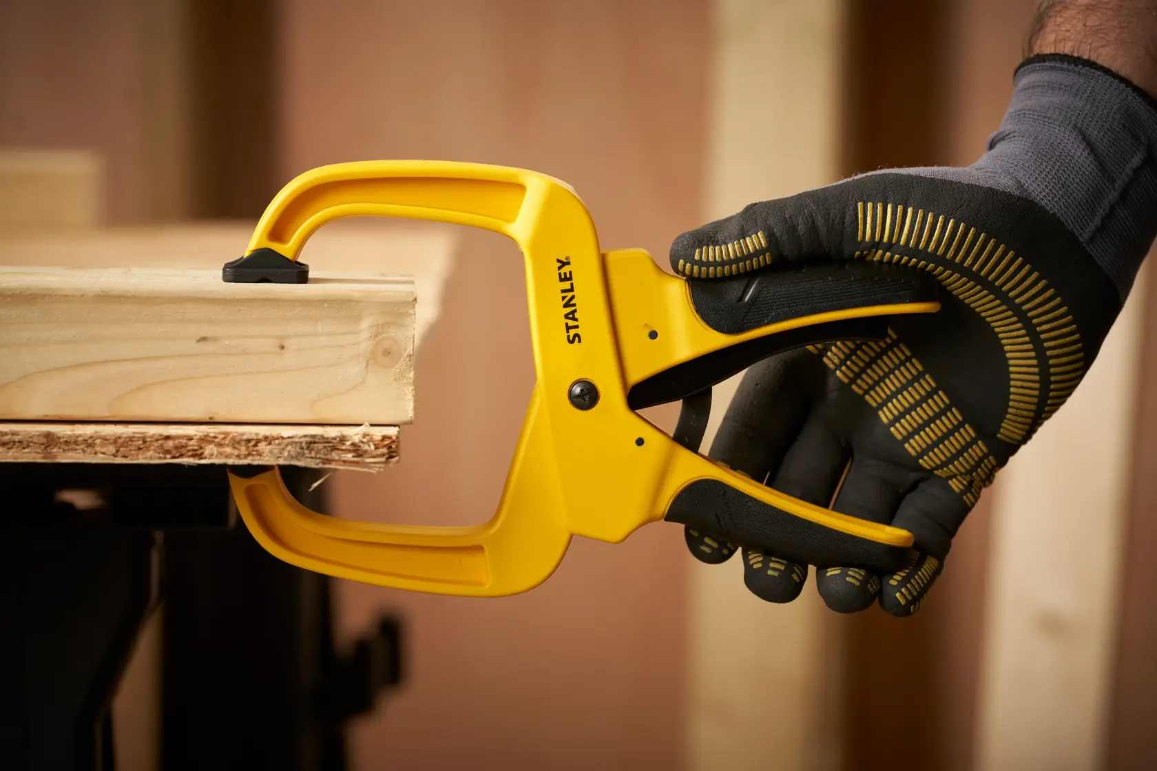 STANLEY STHT0-83200 clamp holding wooden boards, gloved hand operating, product in workshop use.