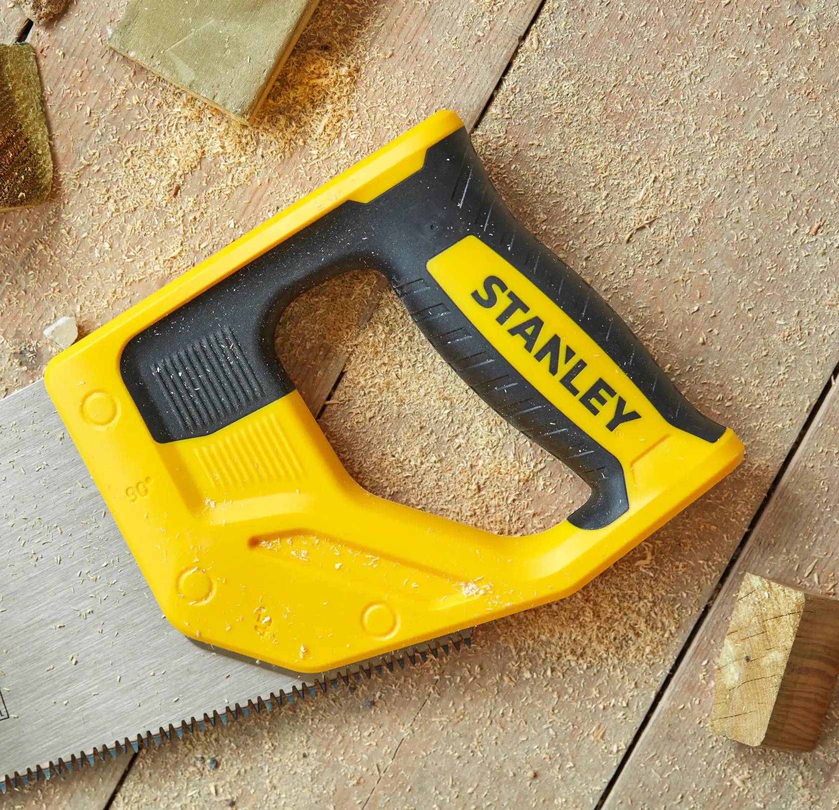 STANLEY STHT1-20353 handsaw with yellow and black ergonomic handle on wood surface with sawdust.