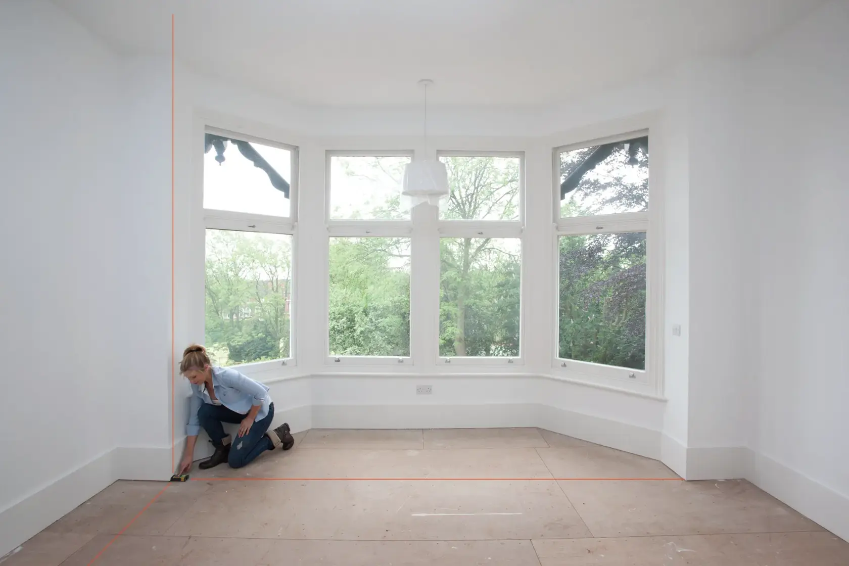 STANLEY STHT1-77139 laser level projecting red lines in bright room, person aligning tool on floor, wide angle.