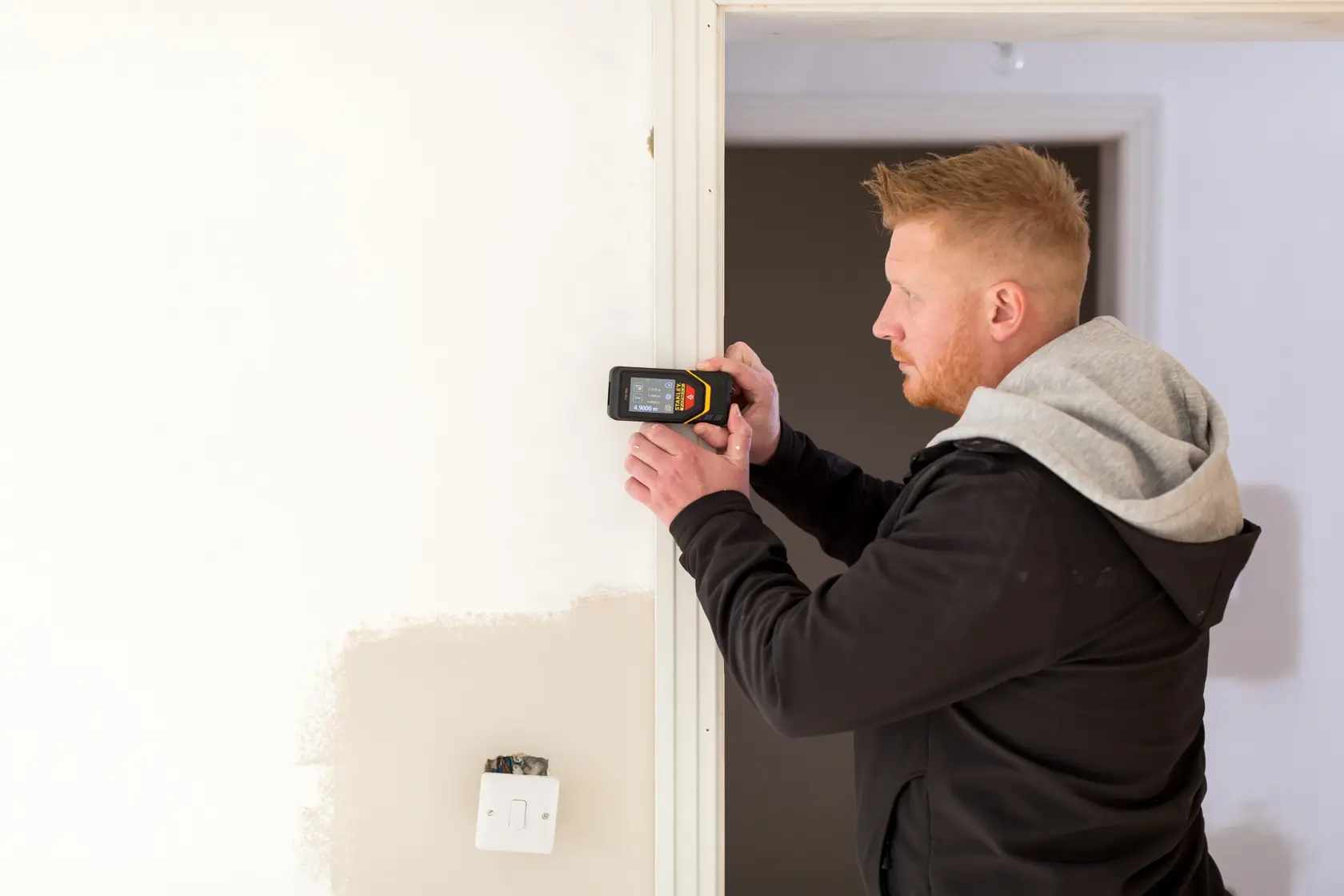Photo of STANLEY STHT1-77139 electronic detector used on a wall, person in black hoodie operating device.