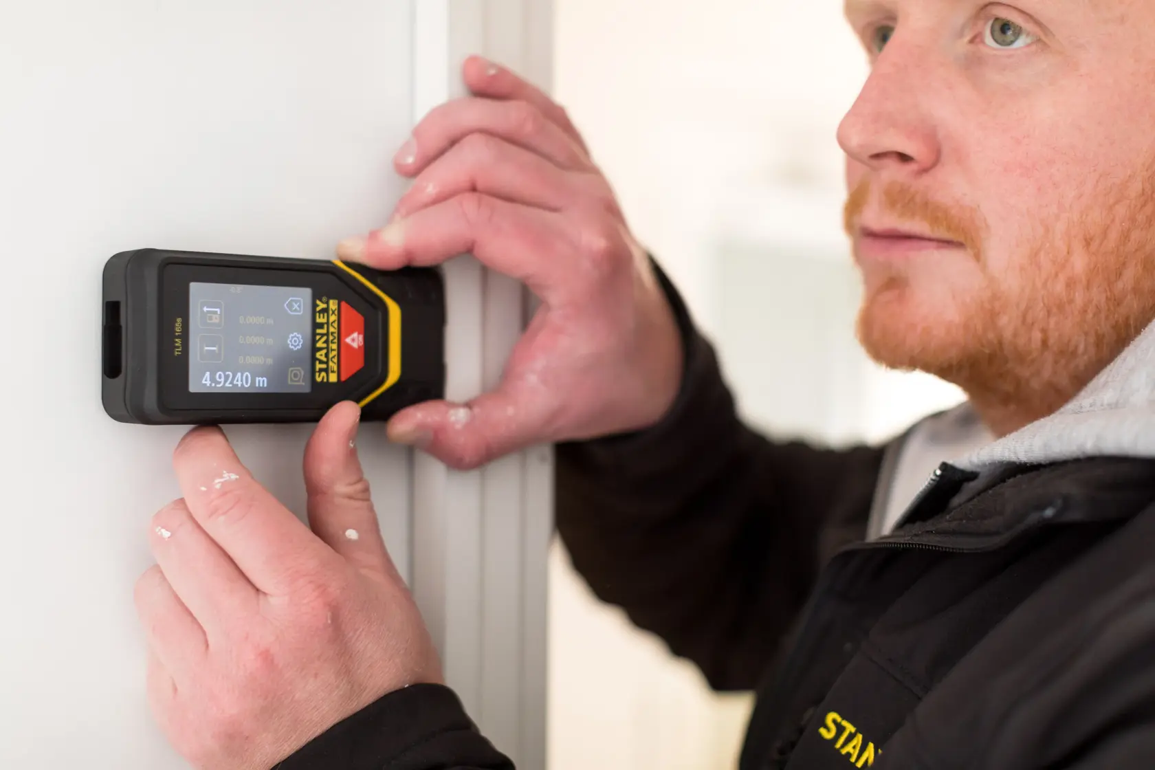 Photo of STANLEY STHT1-77139 laser distance measurer in use against a door frame, display shows measurement.