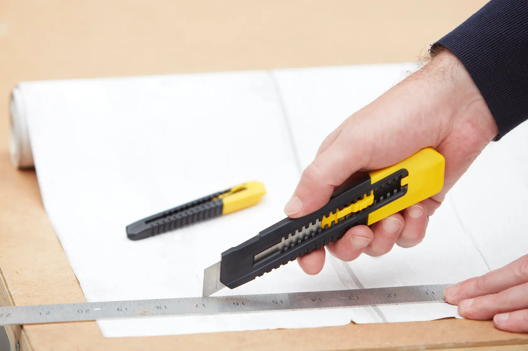STANLEY STHT10202-0 utility knife with black and yellow handle cutting paper along a ruler, second knife in background.