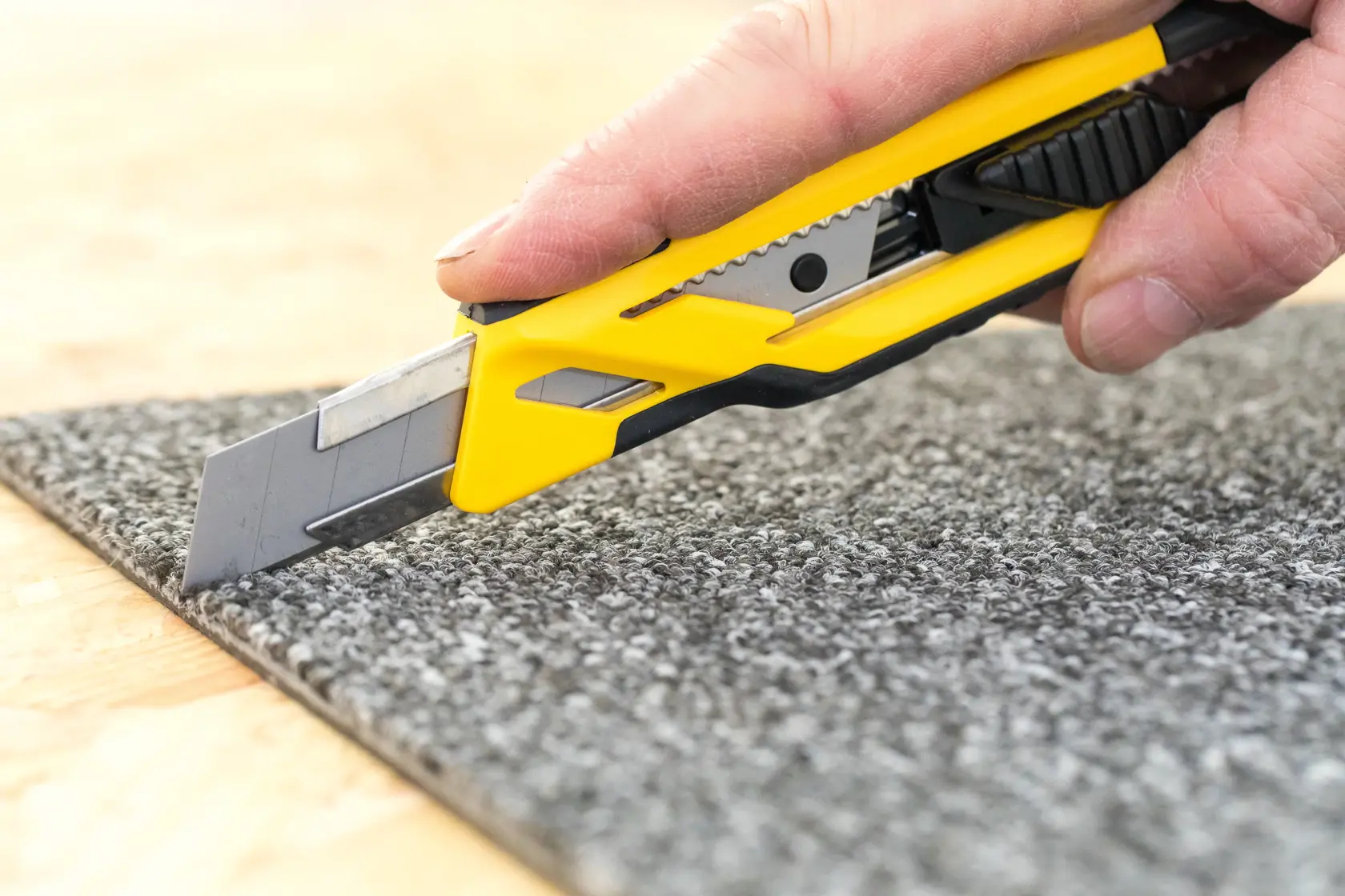 STANLEY STHT10266-0 utility knife with yellow and black handle cutting gray carpet close-up.