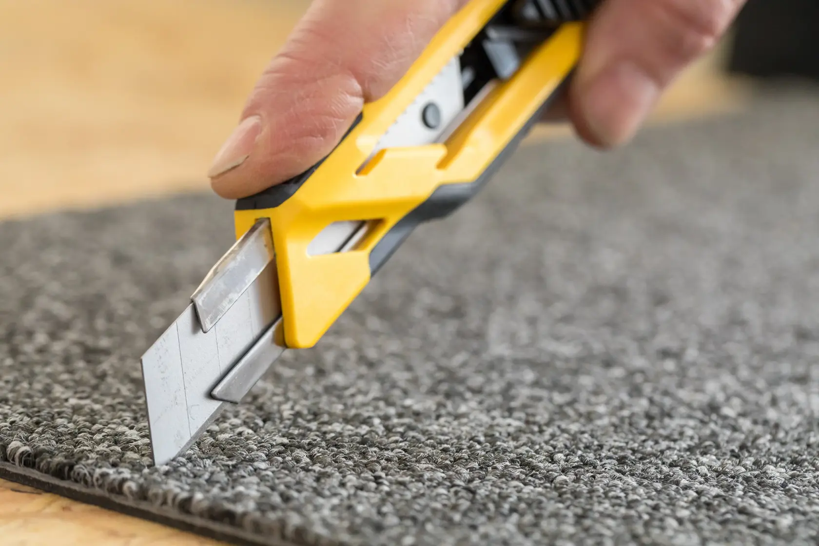 STANLEY STHT10266-0 utility knife cutting grey carpet, close-up photo, yellow and black handle visible.