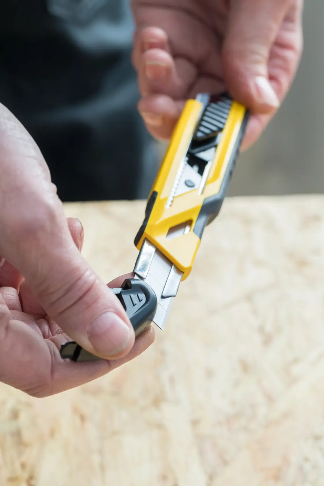 STANLEY STHT10266-0 utility knife with yellow and black body, close-up in hand, blade being adjusted.