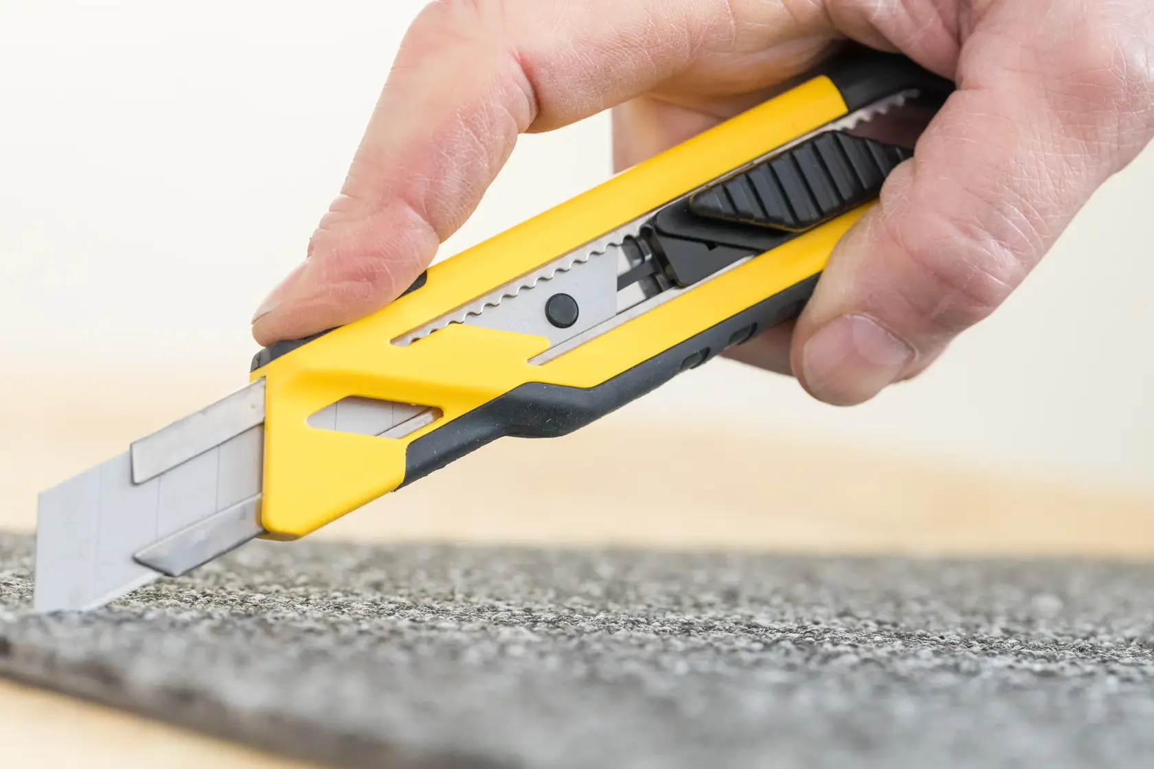 STANLEY STHT10266-1 utility knife with yellow and black body cutting carpet, close-up photography.