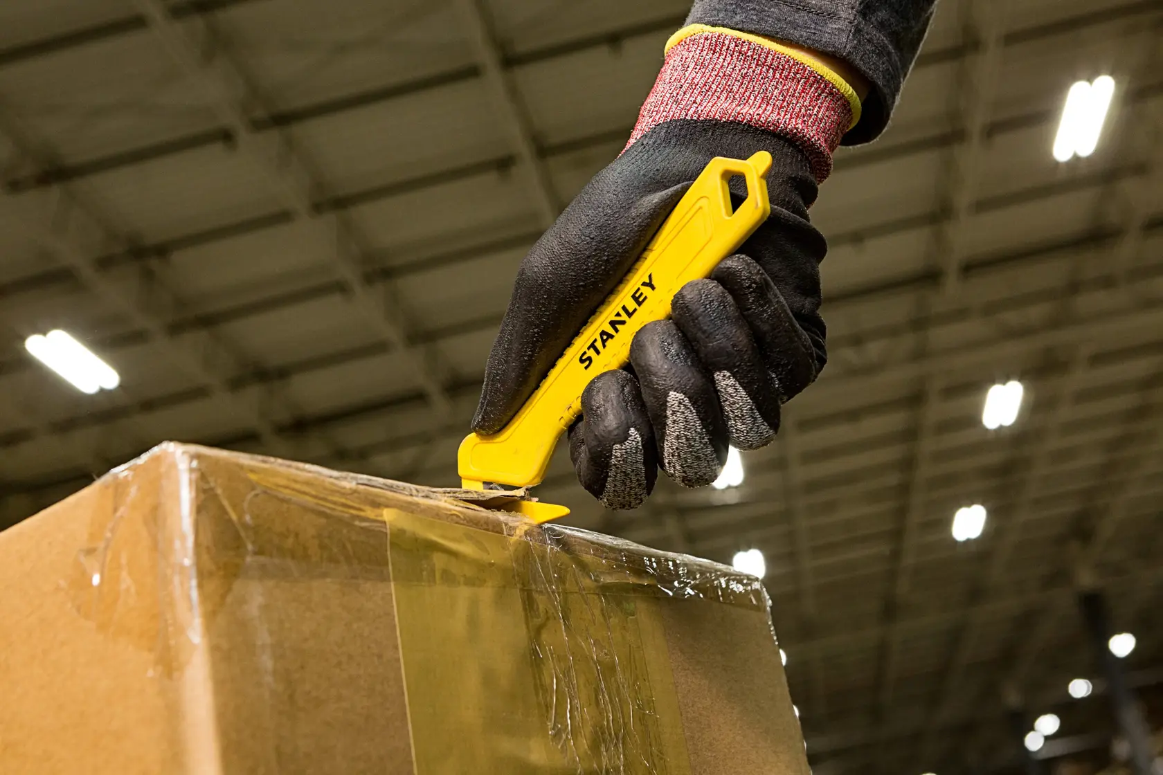 Stanley STHT10355-1 yellow safety utility knife used to cut box tape, close-up photography.