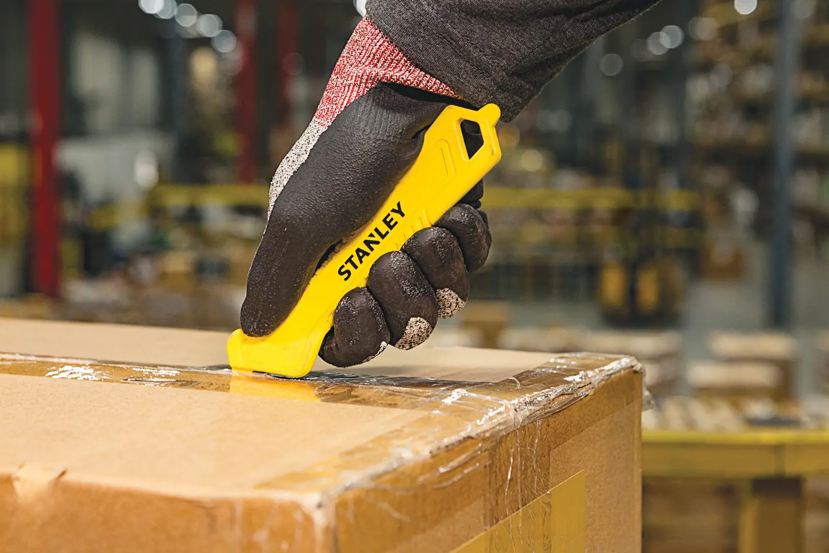 STANLEY STHT10355-1 safety utility knife cutting tape on a cardboard box in a warehouse, close-up.