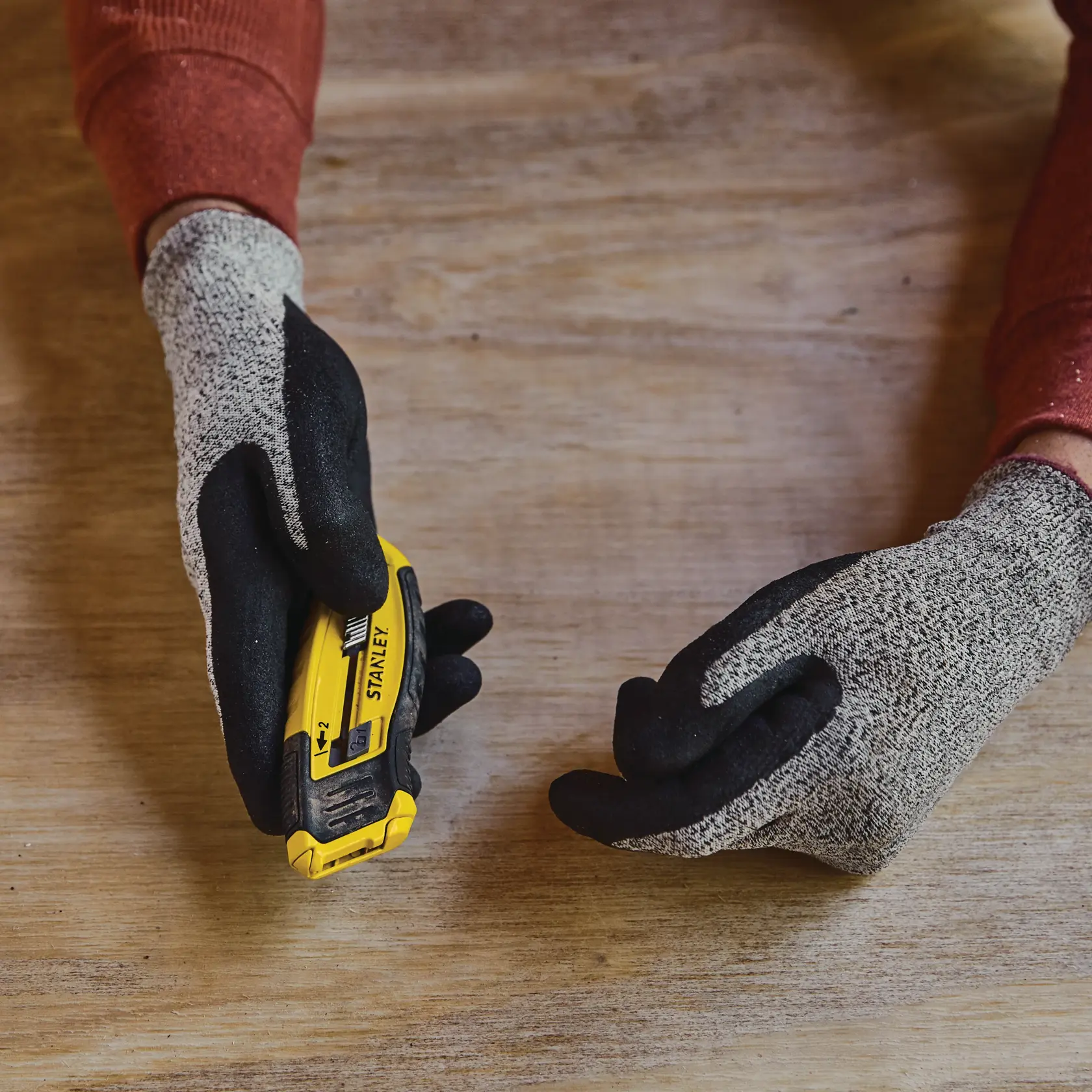 Photo of STANLEY STHT10432-0 utility knife held in gloved hand on wooden surface.