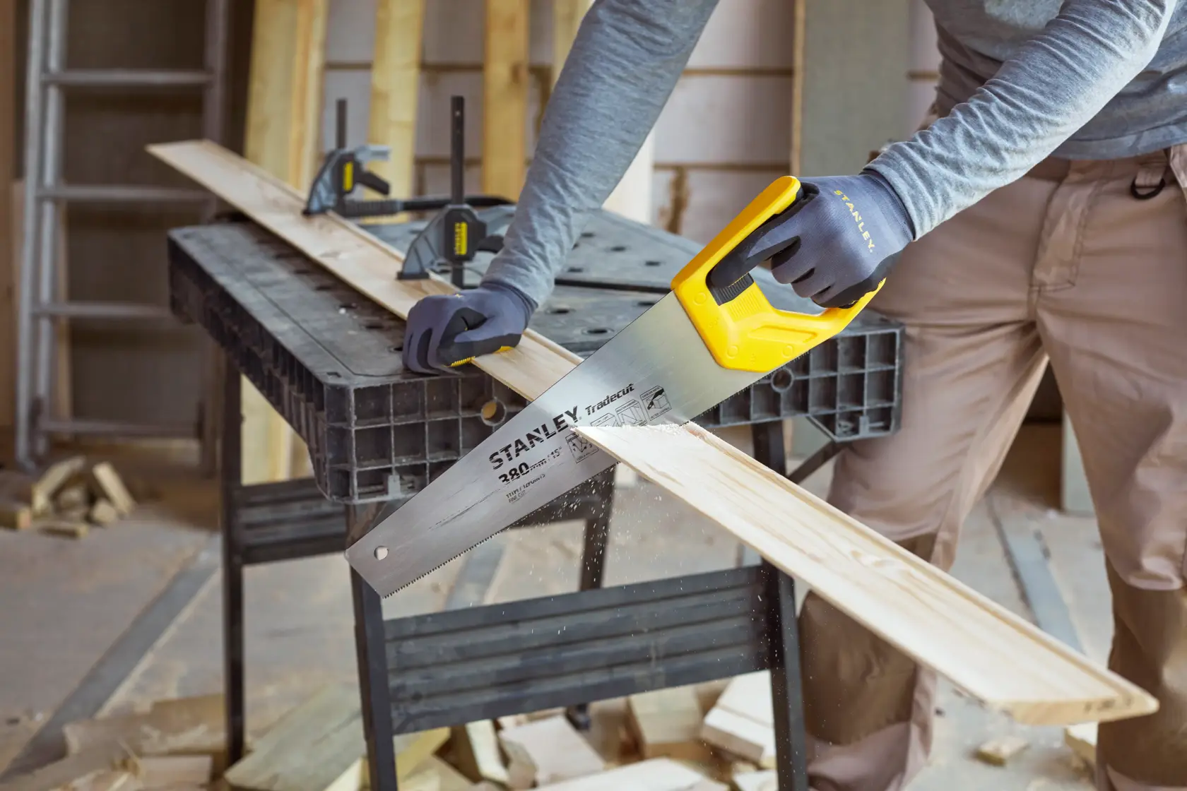 Stanley STHT20349-1 hand saw with yellow handle cutting wood plank on workbench, close-up angle.