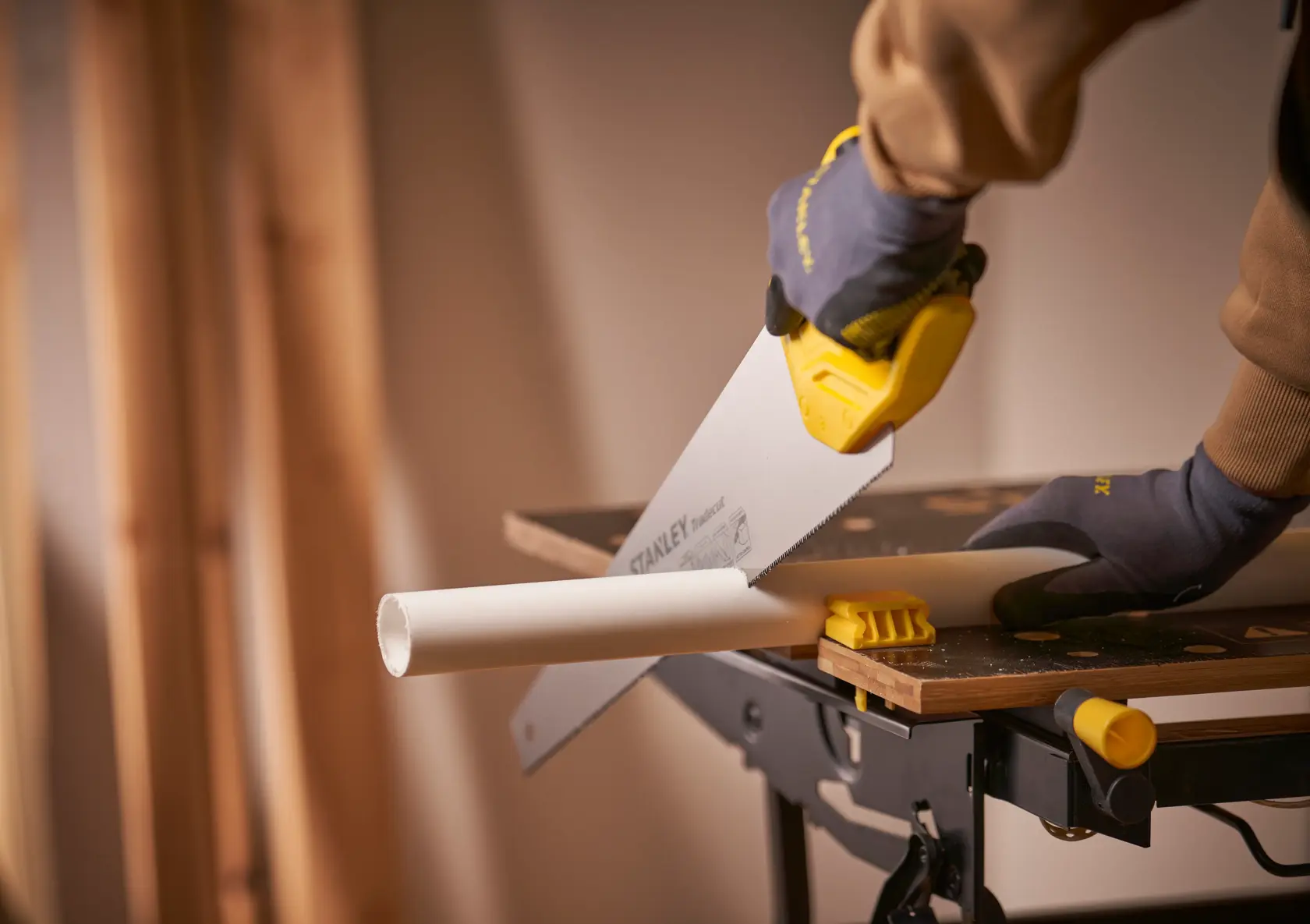 STANLEY STHT20351-1 hand saw cutting white pipe on workbench, close-up photography.