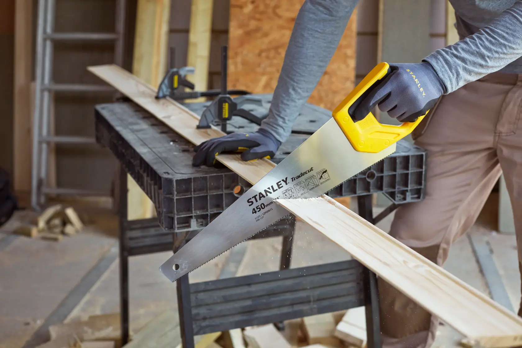 Stanley STHT20355-1 hand saw in use cutting wood, yellow handle, carpentry workspace.
