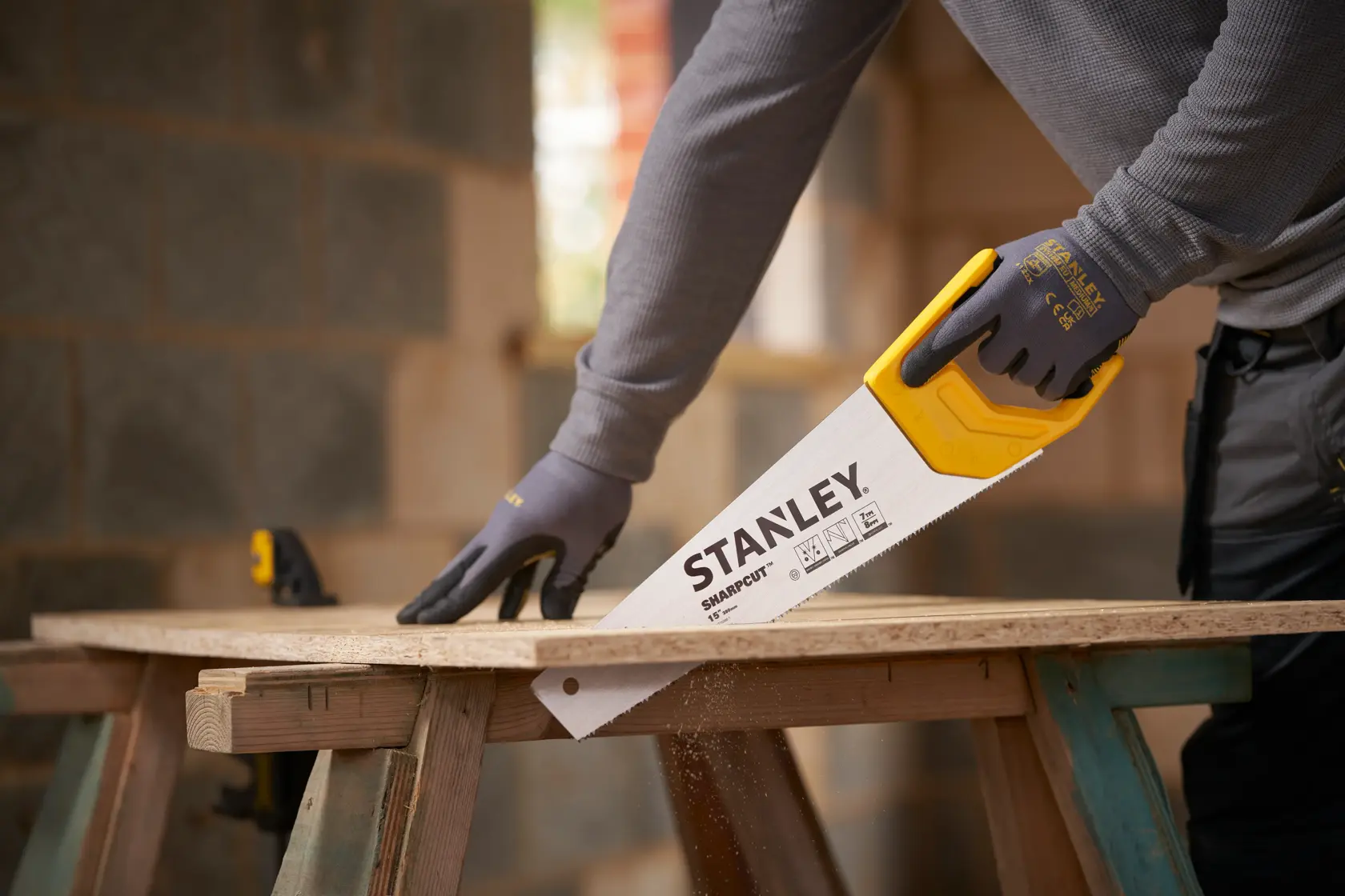 Photo of STANLEY STHT20366-1 hand saw with yellow handle cutting wood, used by a person wearing gloves.