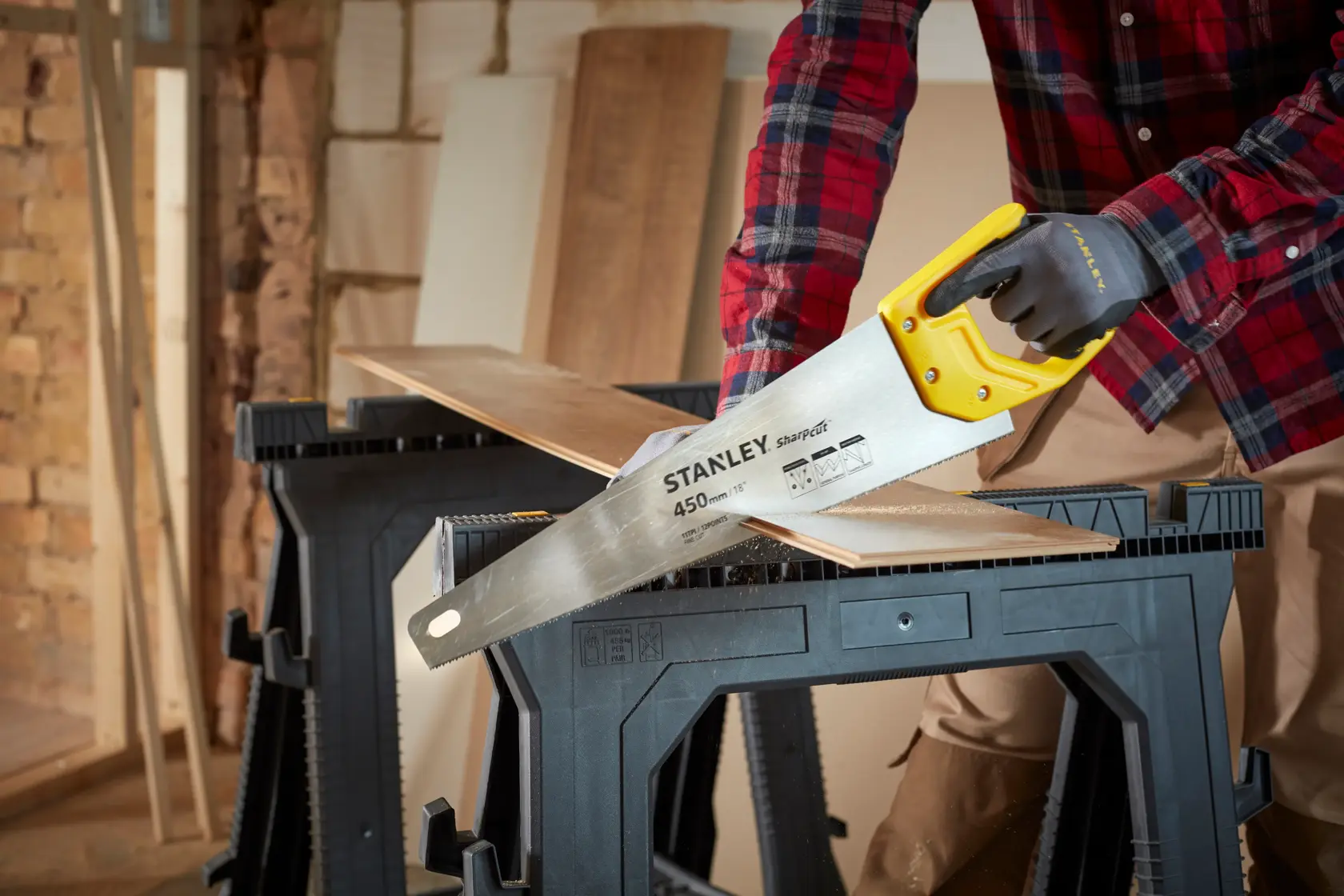 STANLEY STHT20370-1 hand saw with yellow handle cutting wood, photography of product in workshop setting.