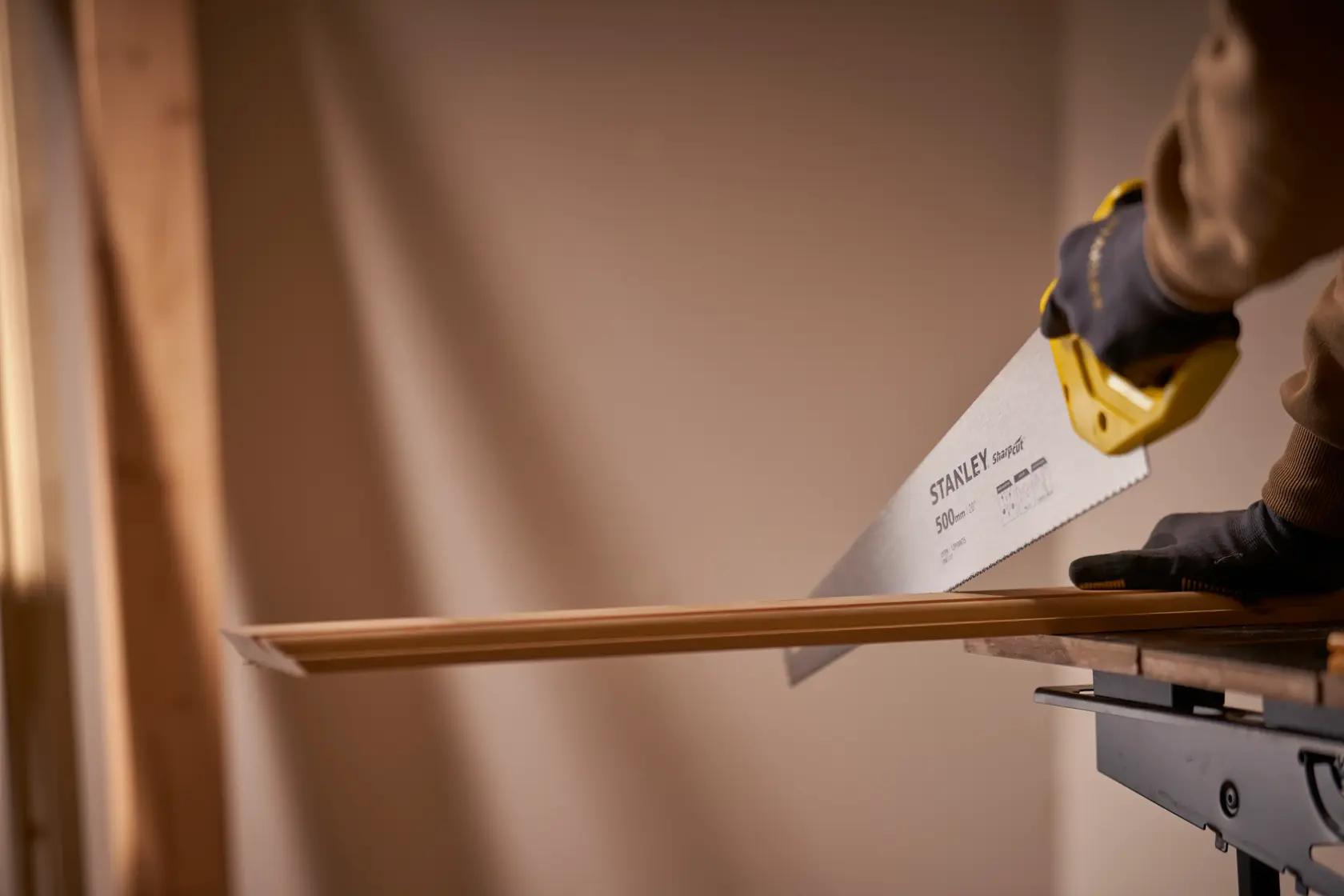 Photo of STANLEY STHT20371-1 hand saw cutting wood, yellow handle and gloved hand, indoor workspace.