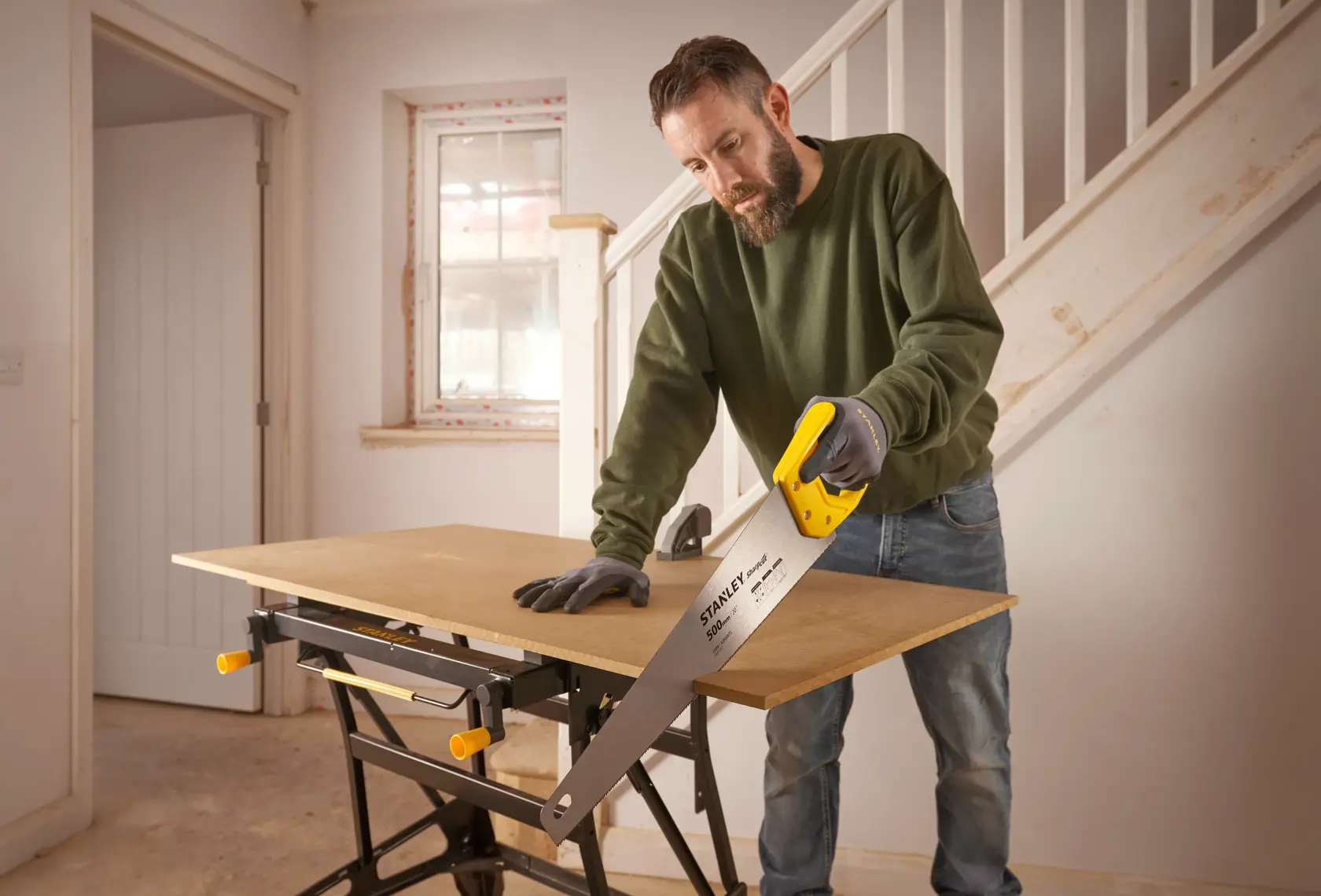 Stanley STHT20371-1 hand saw with yellow handle used for cutting wood on a workbench indoors.
