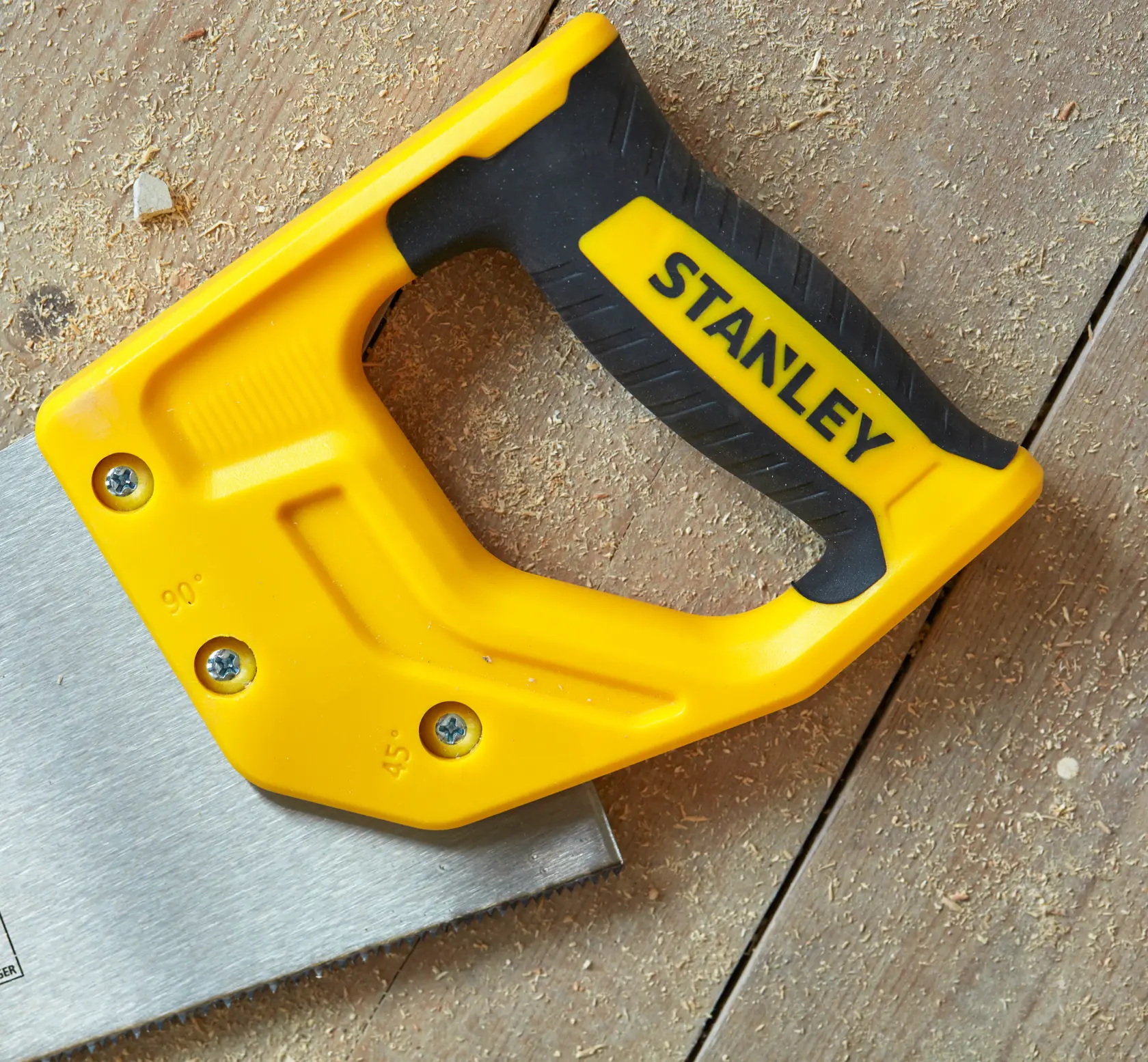 STANLEY STHT20371-1 hand saw with yellow and black handle on wooden surface, close-up angle.