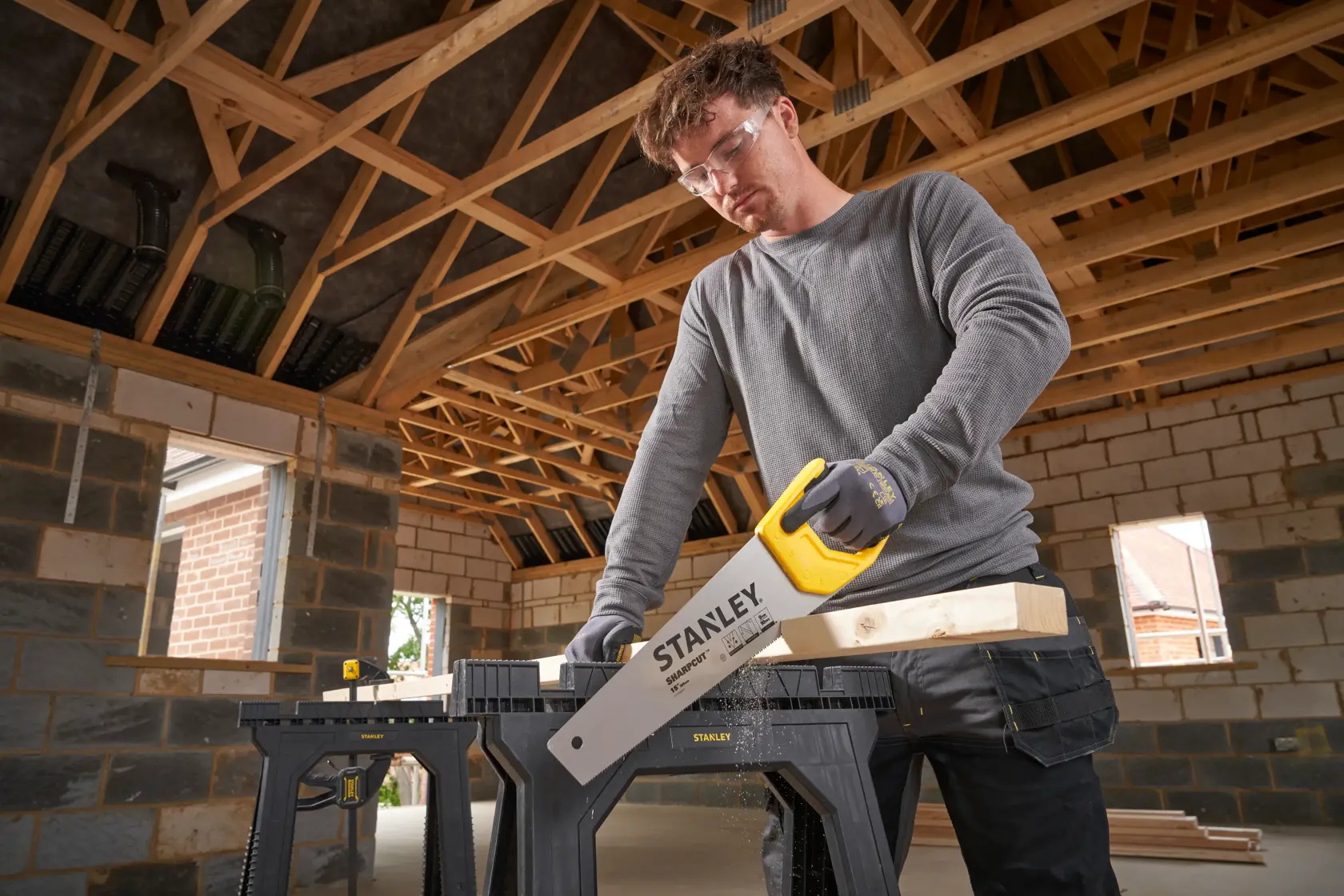 STANLEY STHT20373-1 hand saw with yellow handle cutting wood in workshop setting.