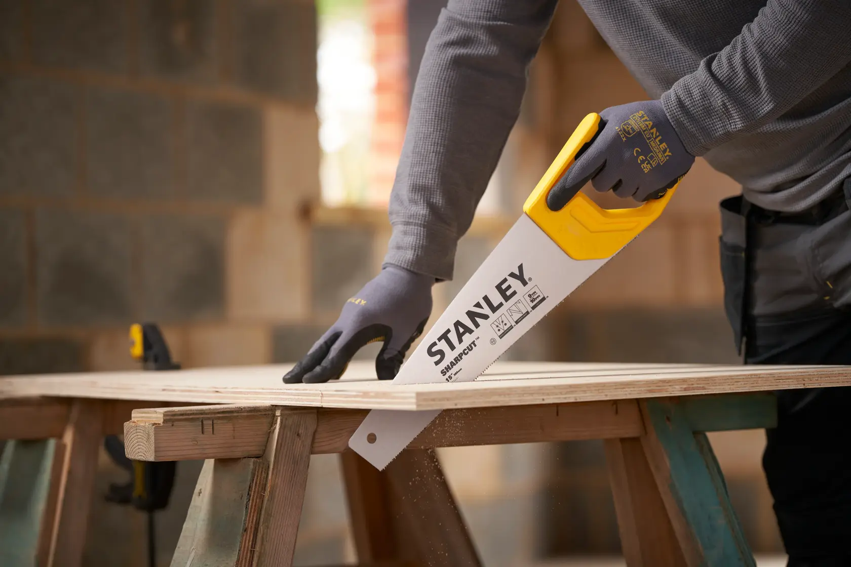 STANLEY STHT20373-1 handsaw with yellow handle cutting plywood, shown in use on a wooden workbench.