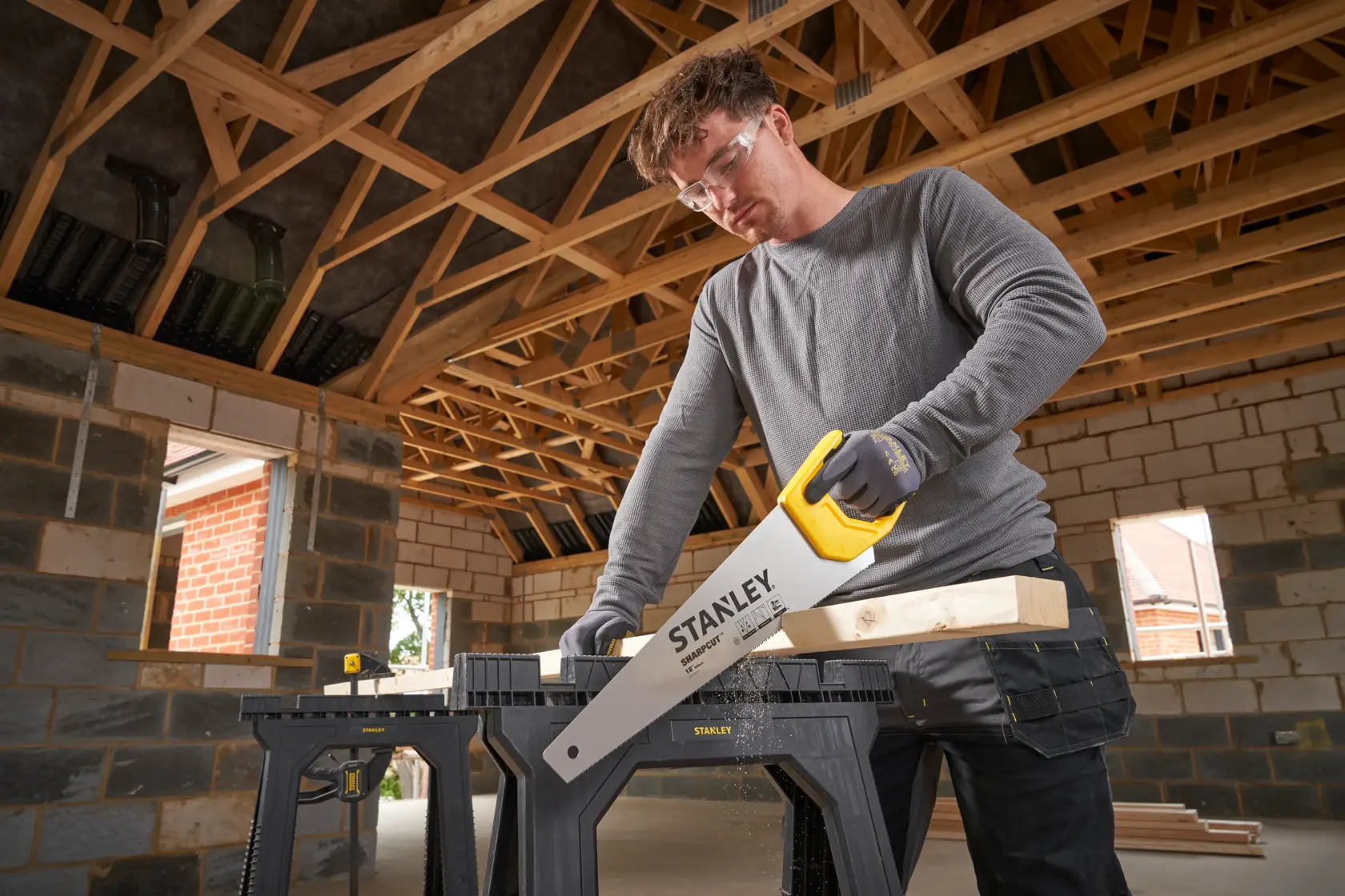 STANLEY STHT20374-1 hand saw with yellow handle cutting wood on black sawhorse in construction site.