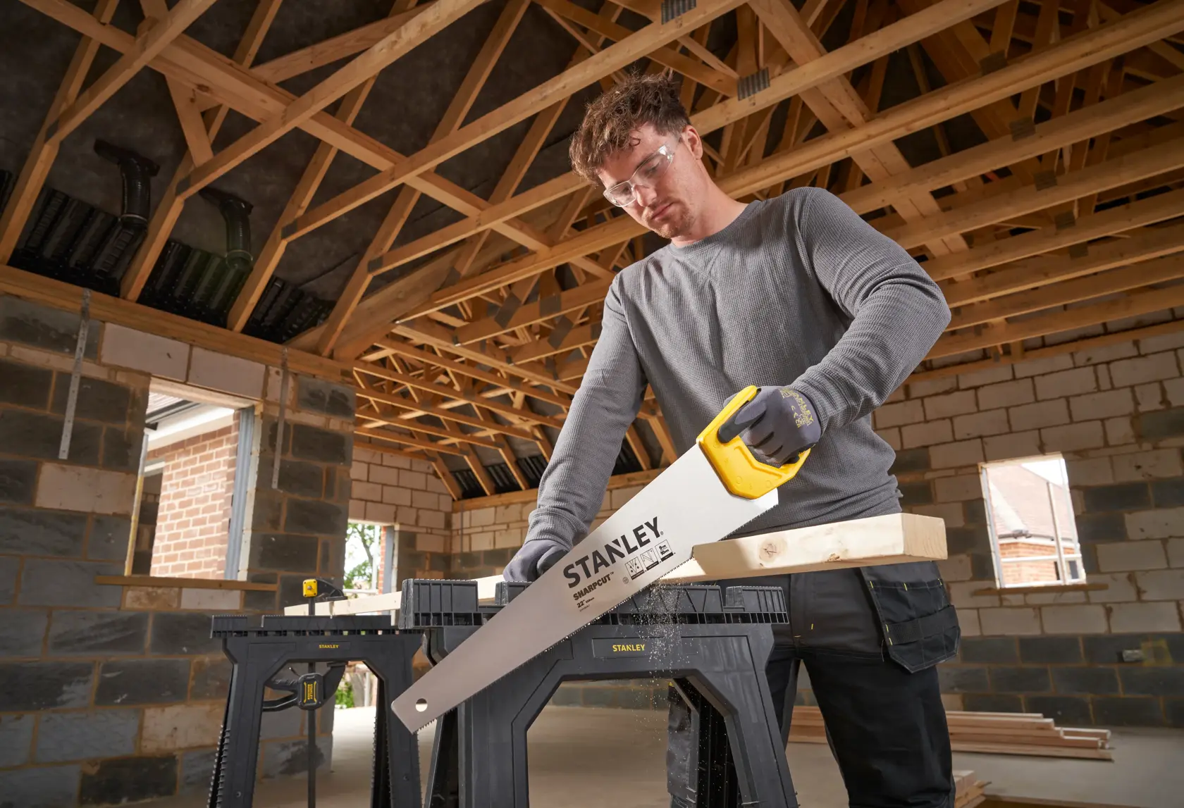 Photo of STANLEY STHT20376-1 hand saw with yellow handle cutting wood on construction site.