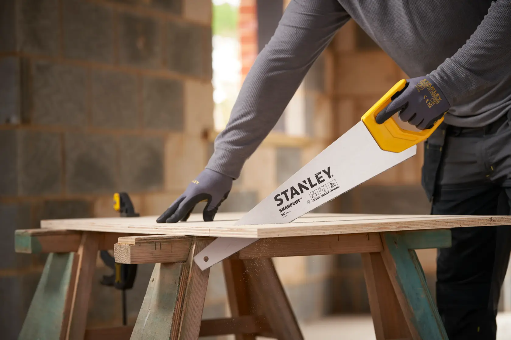 Photo of STANLEY STHT20376-1 hand saw with yellow handle cutting wood in a workshop setting.