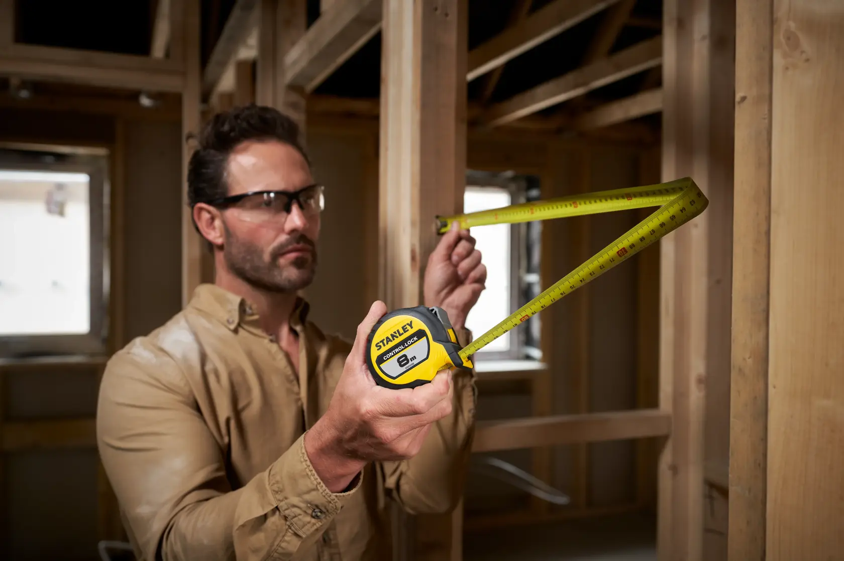 STANLEY® CONTROL-LOCK™ 8M (25mm wide) Tape Measure being used by worker checking measurements on double sided measure on timber frame