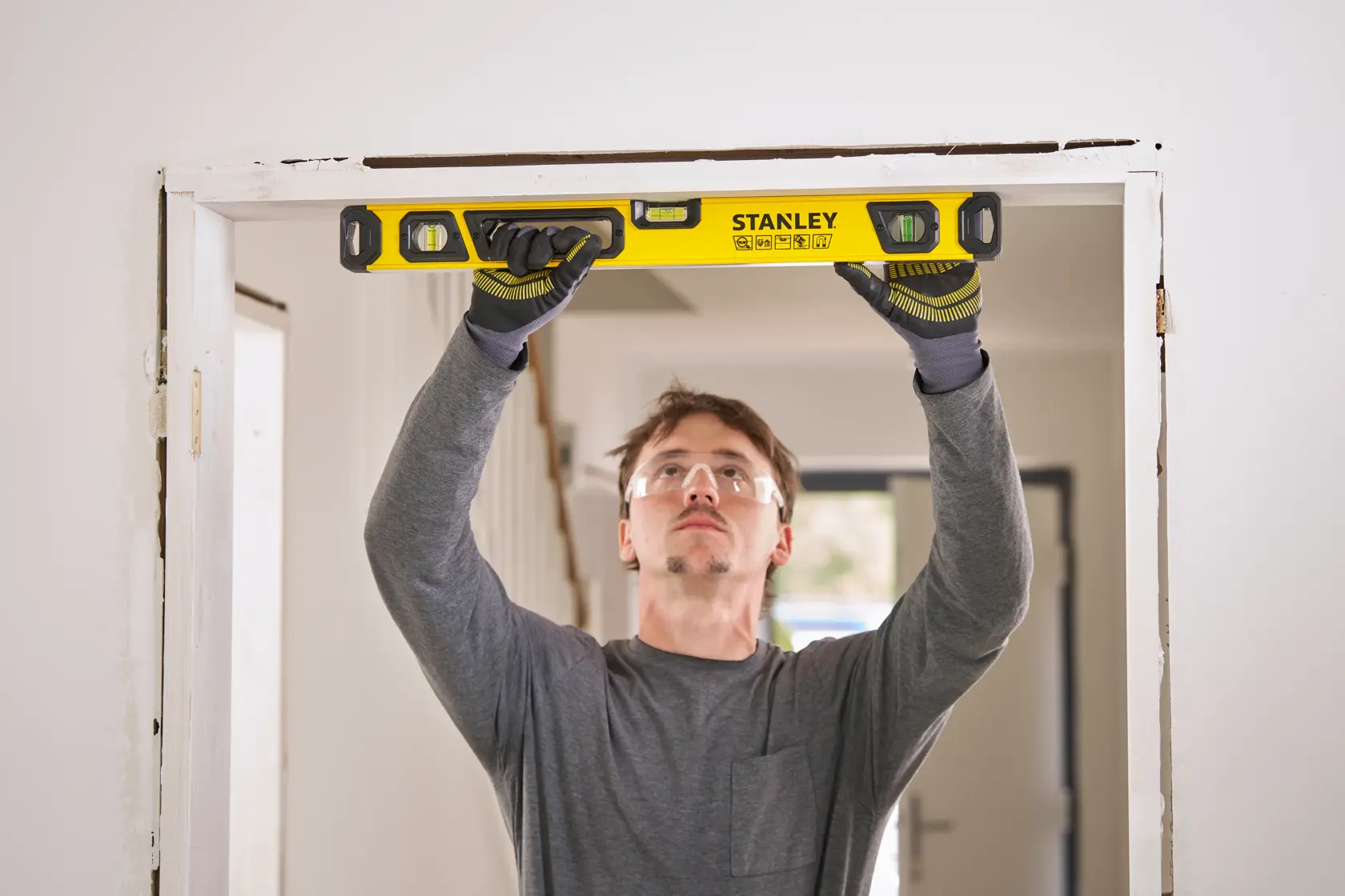 Person using a yellow STANLEY spirit level to check the alignment of a door frame indoors.