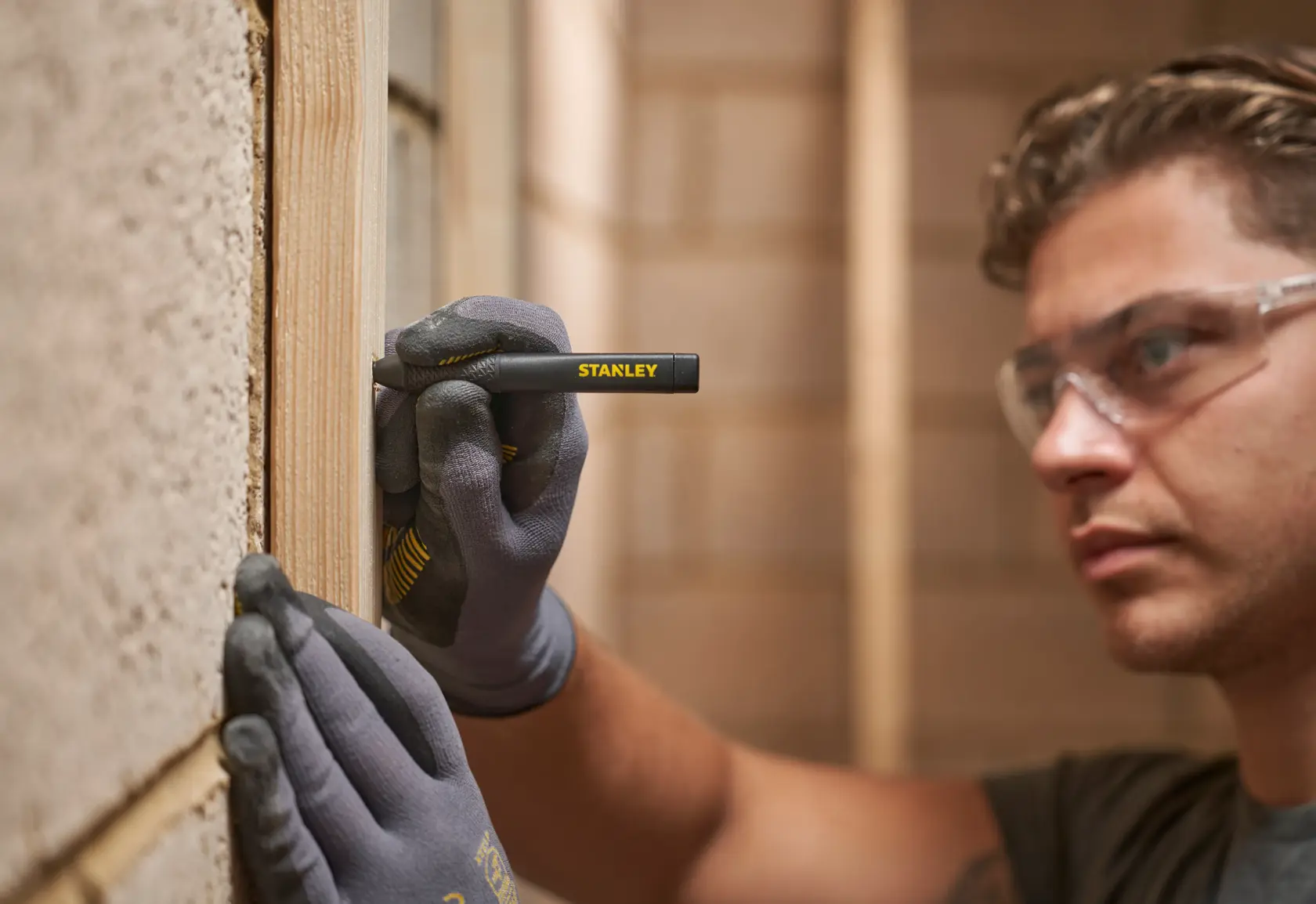 Person wearing gloves uses STANLEY marking pen to draw lines on wood during construction.