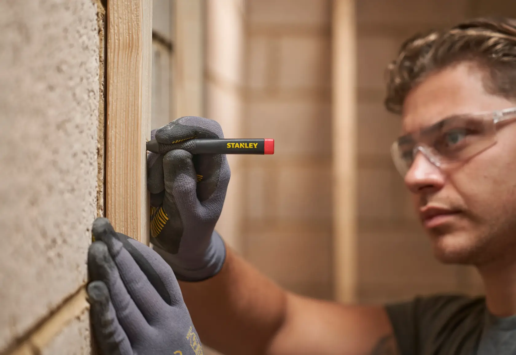 Person marks wood with STANLEY carpenter pencil while wearing gloves and safety glasses.