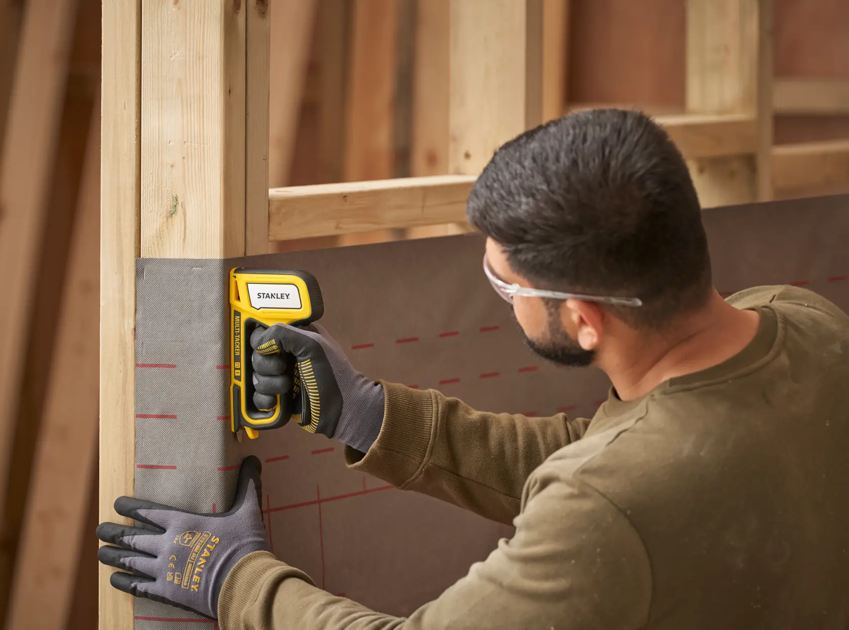 Photo of STANLEY STHT70440-0 stapler being used on wall frame, worker wearing gloves.