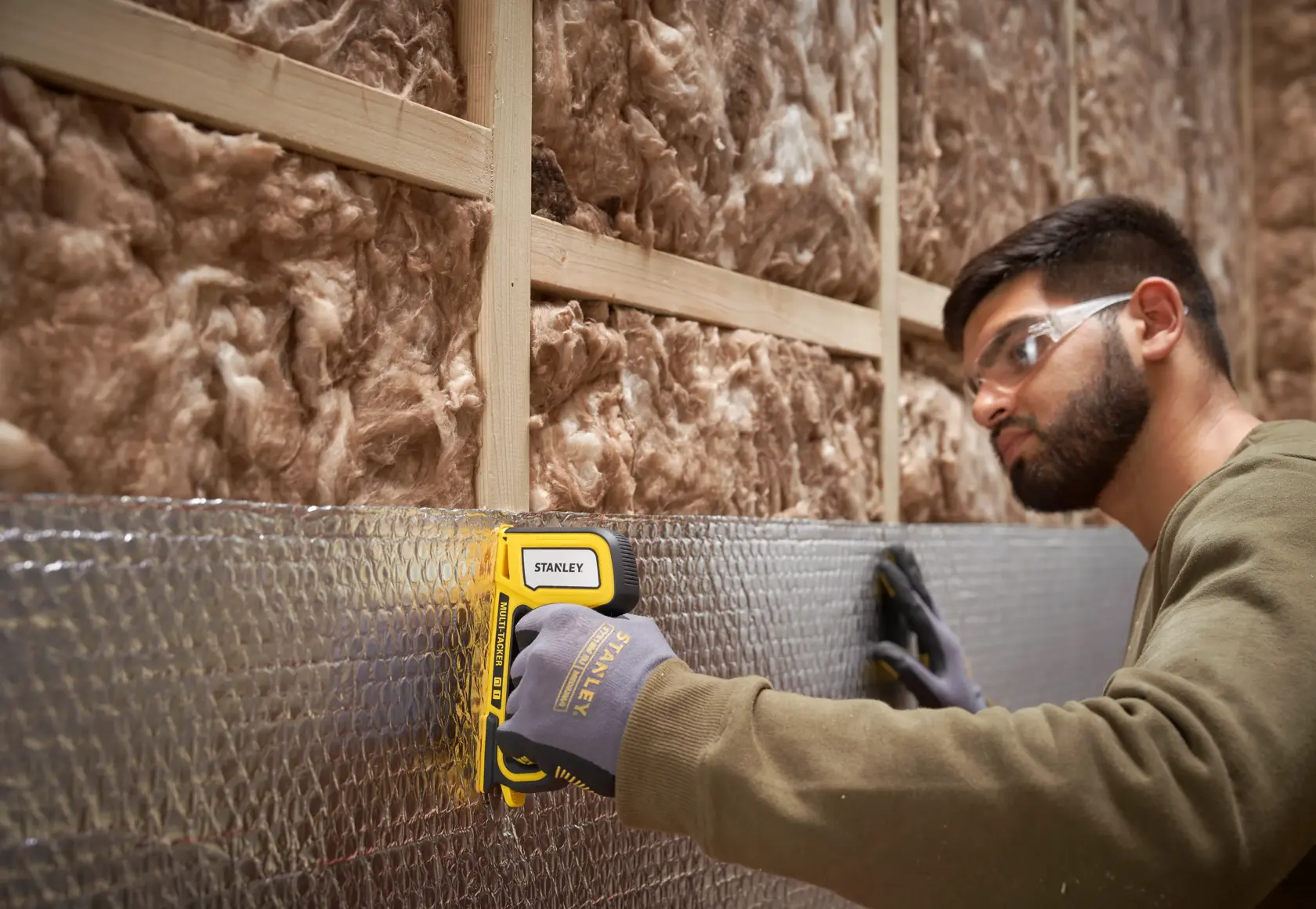 Photo of STANLEY STHT70440-0 staple gun in use attaching foil insulation to a wall frame.