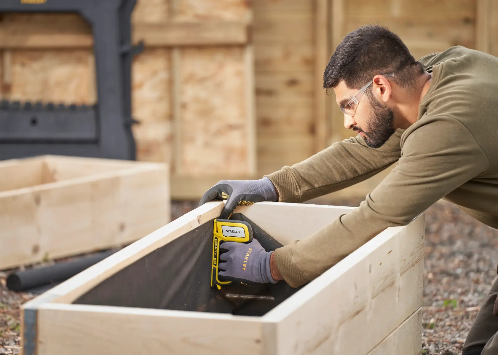 STANLEY STHT70440-0 stapler in use attaching fabric to wooden planter, outdoor setting.