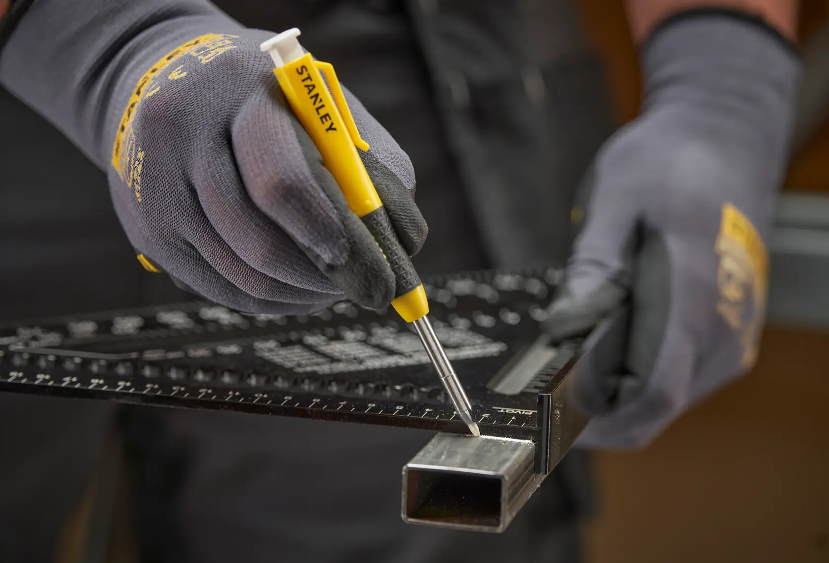Gloved hands use a STANLEY marking tool and ruler to mark metal tubing for measurement or cutting.