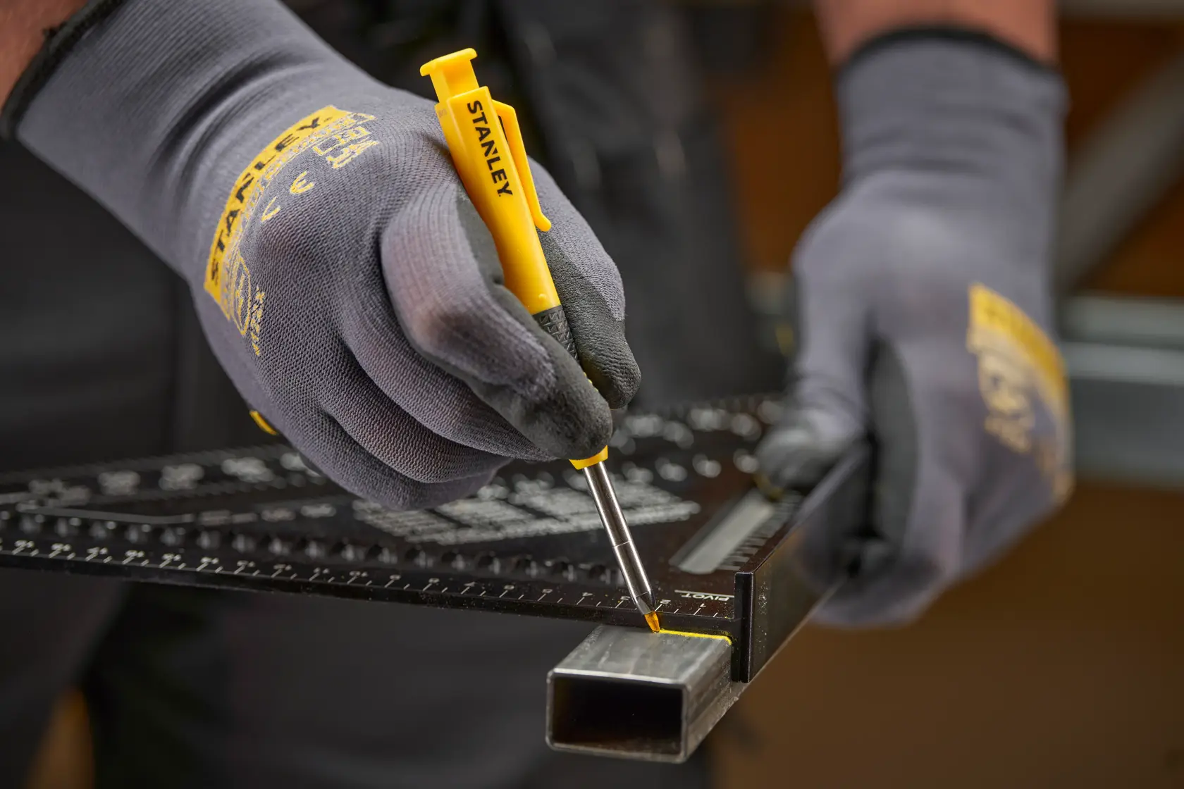 Gloved hands use a yellow STANLEY marking tool with ruler on a metal tube for precise measurement and marking.
