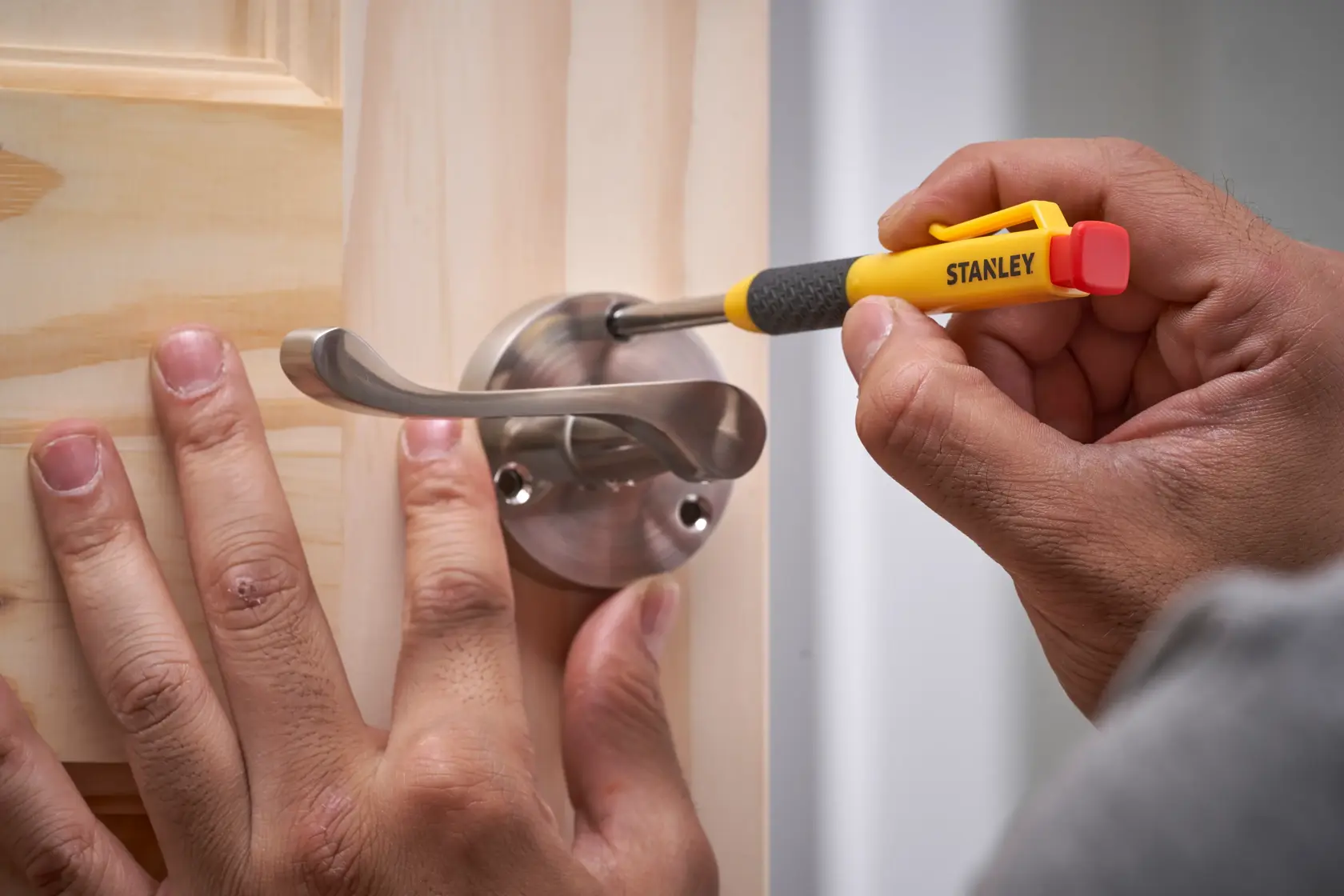 Person uses a Stanley screwdriver to attach a metal door handle to a wooden door.