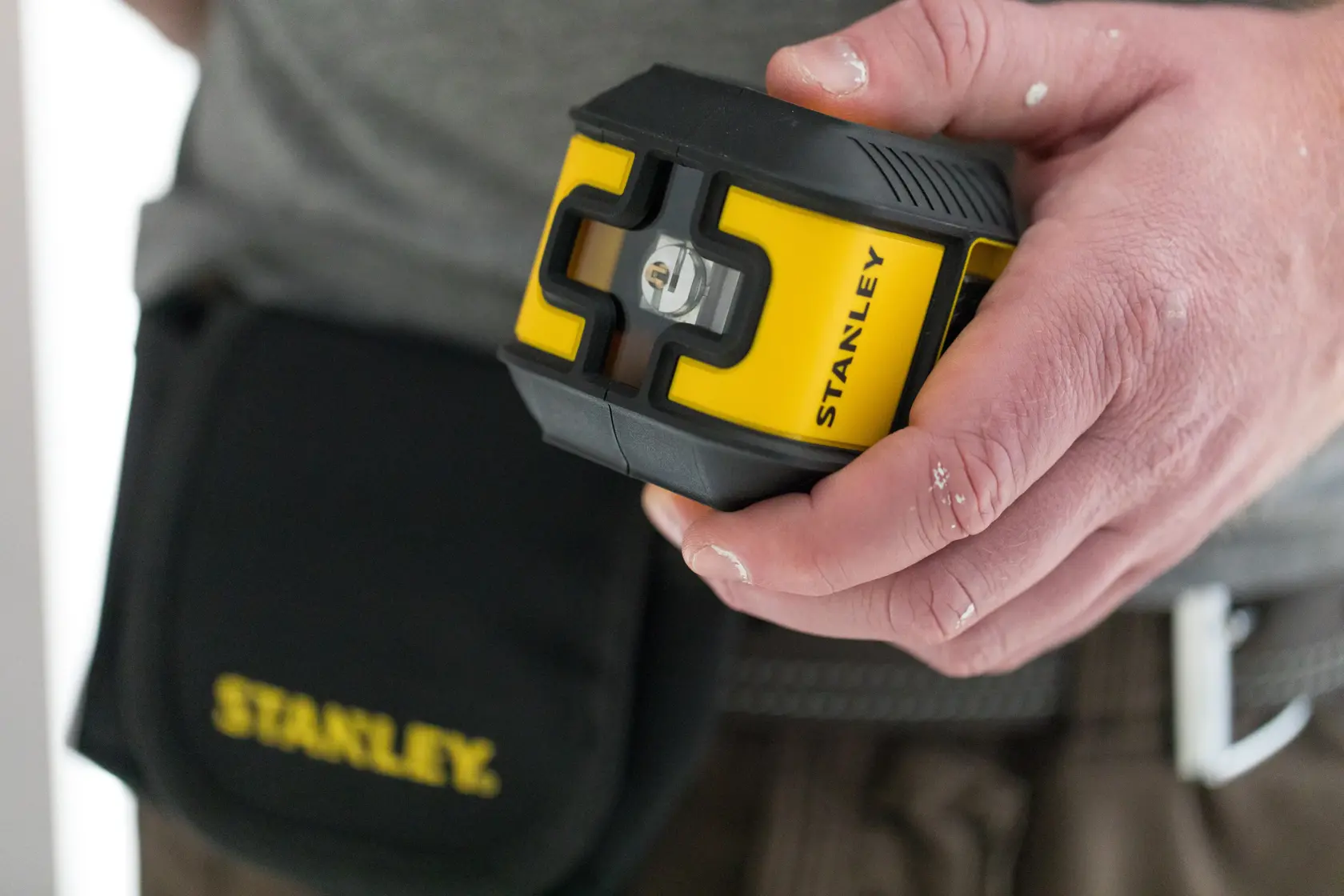 Photo of STANLEY STHT77499-1 laser level tool with black and yellow casing held in hand, tool pouch visible.