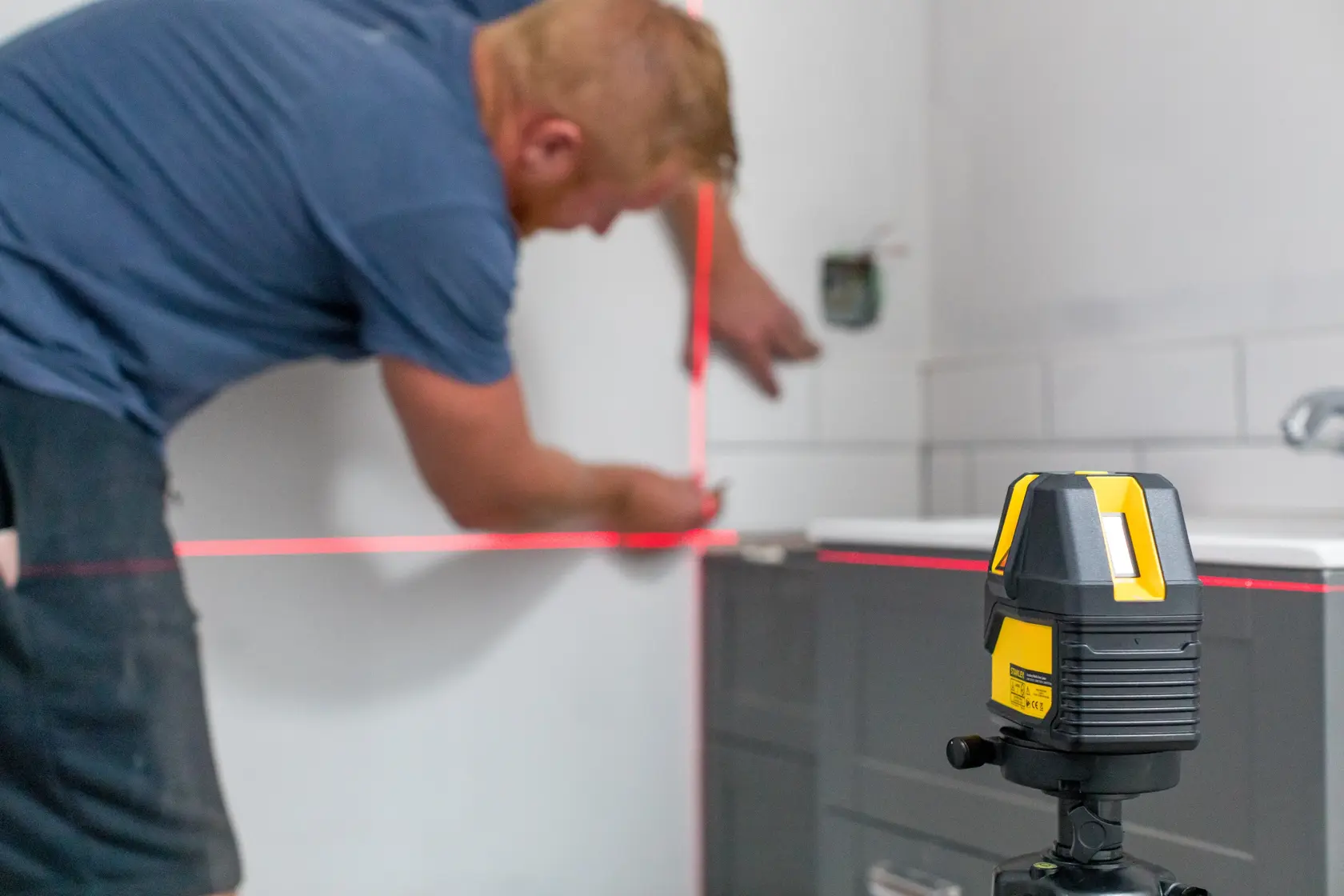 STANLEY STHT77514-1 laser level device projecting red lines for precise wall alignment in a bathroom renovation.