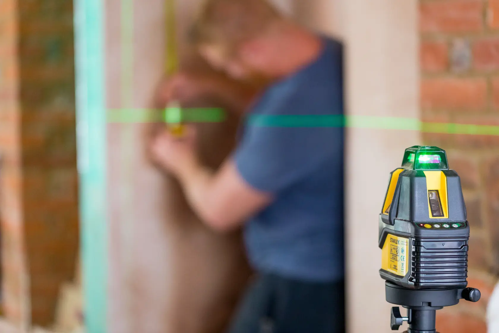 STANLEY STHT77524-1 laser level projecting green line in construction setting, close-up side angle.