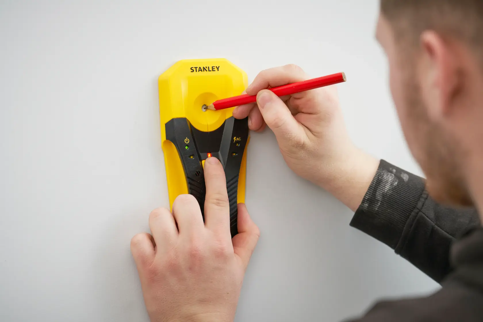 STANLEY STHT77588-0 stud finder used on wall with red pencil marking center, close-up photography.