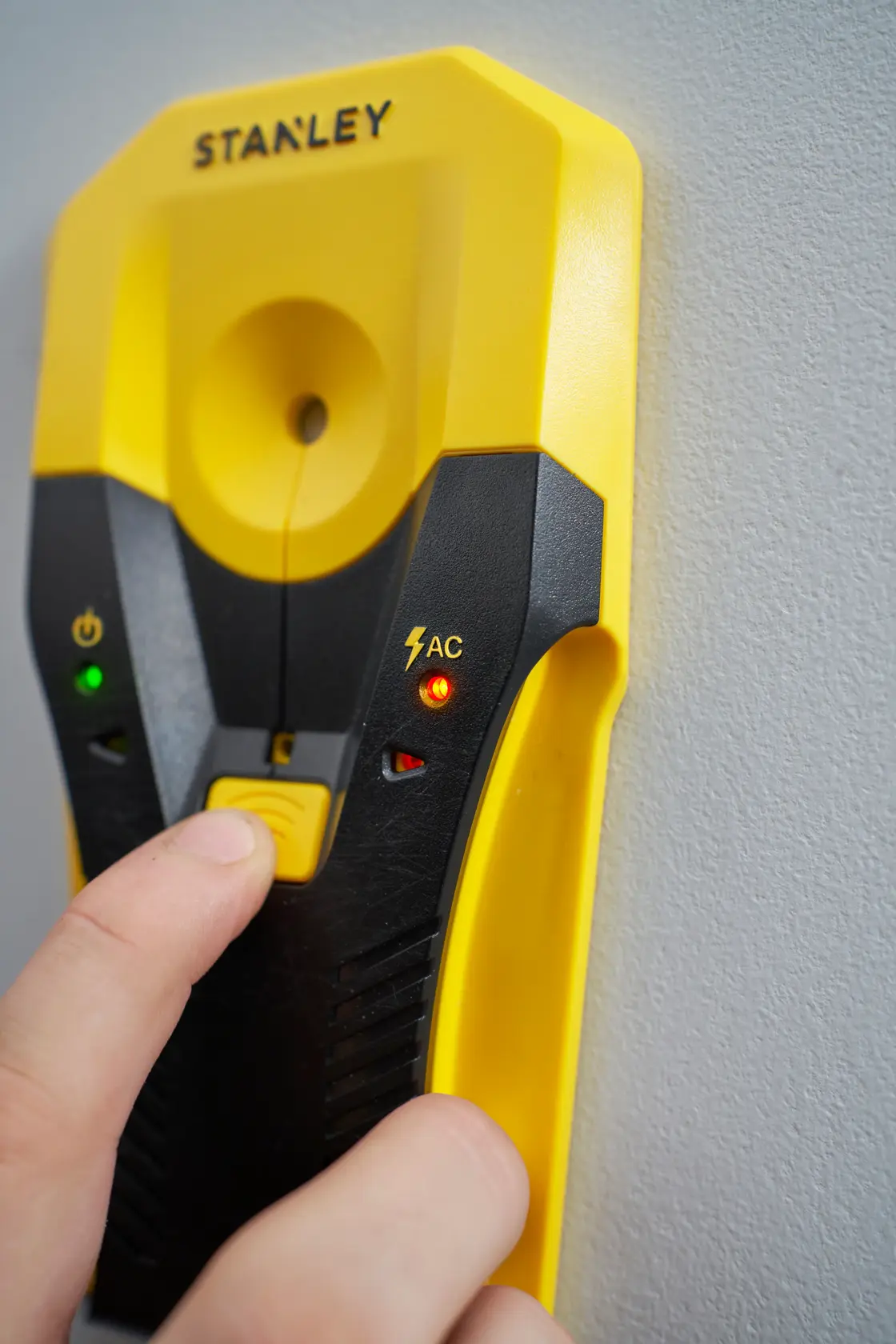 Photo of STANLEY STHT77588-0 digital stud finder against wall, yellow and black hand-held device with indicator lights.